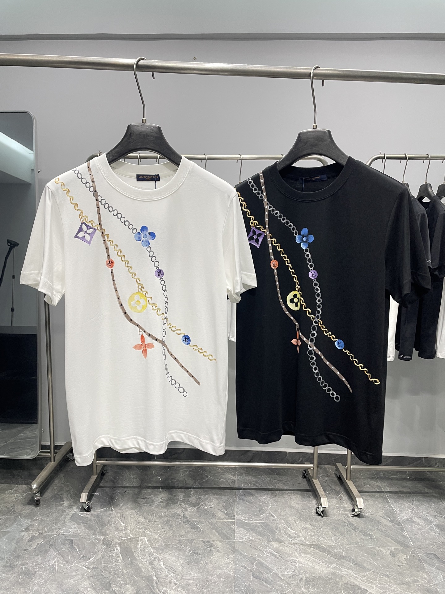 NO:857811,1V26SS new spring and summer chain flower hand-painted cotton round neck short-sleeved T-shirt!  The collision of French light luxury and artistic sense, the perfect integration of brand iconic elements and hand-painted artistic sense, is the finishing touch to highlight taste in daily wear.  It is made of pure cotton fabric, which is soft to the touch and skin-friendly, breathable and comfortable, and has a crisp silhouette. It has no sense of restraint in daily wear and is not easily deformed after washing. It takes into account comfort and durability. You can also feel the delicate skin-friendly experience when wearing it close to the body. The classic round neck cut is neat and generous, not picky about the body shape, available in black and white, and the simple base is decorated with hand-painted chains.  The strips are intertwined with Monogram floral prints, gold, blue, purple and other colors, which are smart and layered; the back is handwritten with gold strokes and paired with a reverse label, which combines a sense of luxury and casual art. It not only retains brand recognition, but also avoids a sense of exaggeration. The overall style is light, luxurious and full of artistic flavor.  It is a versatile item with great personality in the wardrobe. Wear it alone with jeans or casual trousers, it is casual, refreshing and eye-catching. Pair it with a denim jacket, suit jacket or knitted cardigan to create a rich layered look. It can be easily controlled whether it is commuting out, daily leisure or light social occasions. It has both practicality and fashion sense. It is a classic choice that shows the French light luxury taste. Color White, Black Size M-3XL Size Reference M Shoulder Width 43 Chest 100 Clothing Length 69  L size shoulder width 44 bust 104 length 70 XL size shoulder width 45 bust 108 length 71 2 XL size shoulder width 46 bust 112 length 72 3198609091V26SS春夏新款链条花卉手绘纯棉圆领短袖T恤！ 法式轻奢与艺术感的碰撞,将品牌标志性元素与手绘艺术感完美融合,是日常穿搭中彰显品味的点睛之笔. 采用纯棉面料,触感柔软亲肤,透气舒适且版型挺括,日常穿着无束缚感,洗后不易变形,兼顾了舒适度与耐用性,贴身穿也能感受到细腻的亲肤体验.经典圆领剪裁利落大方,不挑身形,黑白两色可选,简约基底上点缀着手绘感链条与Monogram花卉印花,金色、蓝色、紫色等色彩交织,灵动又富有层次；后背则以金色笔触手写字样,搭配反向标签,将奢华感与随性艺术感拉满,既保留了品牌辨识度,又避免了浮夸感,整体风格轻奢又充满艺术气息. 它是衣橱中极具个性的百搭单品,单穿搭配牛仔裤或休闲裤,随性清爽又吸睛；外搭牛仔夹克、西装外套或针织开衫,能打造出层次丰富的造型,无论是通勤出街、日常休闲还是轻社交场合,都能轻松驾驭,实穿性与时尚感兼备,是彰显法式轻奢品味的经典之选. 颜色白色、黑色 尺码M-3XL 尺寸参考 M码肩宽43胸围100衣长69 L码肩宽44胸围104衣长70 XL码肩宽45胸围108衣长71 2XL码肩宽46胸围112衣长72 3XL码肩宽47胸围116衣长73,,jeans,jackets & coats,jackets & coats,T-shirt,tees，t-shirt,business suit,,Men's clothing