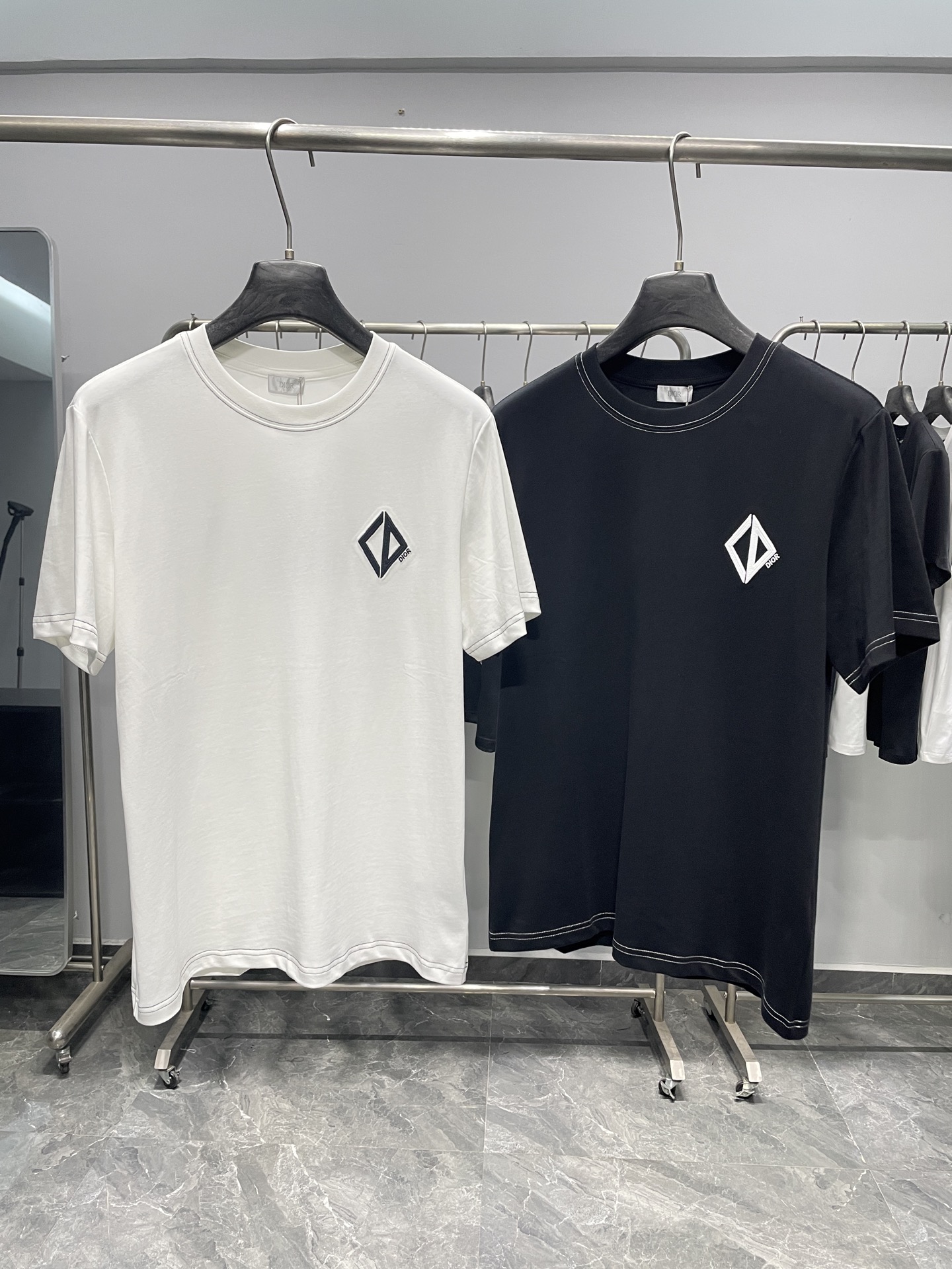 NO:857800,CD26SS new spring and summer CD geometric logo embroidered pure cotton round neck short-sleeved T-shirt!  Minimalist and high-end, the first choice for urban elites!  Carrying the brand's high-end genes with minimalist design, it is a timeless luxury basic item in the wardrobe.  The brand's iconic CD geometric rhombus logo is presented on the left chest with exquisite embroidery technology, and is matched with letter embroidery of the same color, which is low-key but highly recognizable. The collar, cuffs and hem are designed with two-color topstitch piping, which outlines neat lines on a solid color base. Available in black and white, suitable for different wear  Match the scene and style preference. The high-count cotton fabric imported from Italy is selected, which has a delicate touch and skin-friendly feel, excellent breathability and perspiration, and is not easy to deform and wrinkle after long-term wear. The smooth stitching process and solid fabric weight take into account comfort and stiffness, and the upper body has a full drape feeling, showing the texture of high-end ready-made clothing.  It is a representative item of 'light luxury minimalist style'. It abandons exaggerated decoration and uses details to convey taste. It is not only suitable for smart occasions such as business commuting, but also can control the relaxed atmosphere of casual outings. It is the core choice of urban elites and minimalists. It can be used daily.  Pair with straight trousers or casual trousers and white shoes to create a refreshing and smart look. When commuting, wear a minimalist blazer for a more calm and elegant look. For street style wear, you can layer thin metal necklaces with cargo shorts and dad shoes to easily unlock a variety of high-end looks.  Color white, black Size S-XXL Size reference S size shoulder width 43 bust 100 length 69 M size shoulder width 44 bust 104 length 70 L size shoulder width 45 bust 108 length 71 XL size shoulder width 46 bust 112 length 72 2XL size shoulder width 47 bust 116 length 73,, shorts,jackets &  coats,T-shirt,tees,t-shirt,business suit,necklace,19860909CD26SS春夏新款CD几何标识刺绣纯棉圆领短袖T恤！ 极简高级感,都市精英穿搭首选！以极简设计承载品牌高级基因,是衣橱里永不过时的奢品基础款. 左胸以精致刺绣工艺呈现品牌标志性CD几何菱形标识,搭配同色系字母刺绣,低调却极具辨识度.领口、袖口及下摆采用双色明线滚边设计,在纯色基底上勾勒出利落线条,黑白双色可选,适配不同穿搭场景与风格偏好.甄选意大利进口高支棉面料,触感细腻亲肤,透气排汗性优异,久穿不易变形起皱.平整的车线工艺与扎实的面料克重,兼顾舒适感与挺括度,上身垂坠感十足,尽显高级成衣质感. 它是“轻奢极简风”的代表单品,摒弃夸张装饰,用细节传递品味,既适合商务通勤的干练场合,也能驾驭休闲出街的松弛氛围,是都市精英、极简主义者的穿搭核心选择.日常可搭配直筒西裤或休闲裤与小白鞋打造清爽干练造型,通勤时外搭极简西装外套更显沉稳大气,街头风穿搭则可叠戴细款金属项链,搭配工装短裤与老爹鞋,轻松解锁多元高级感造型. 颜色白色、黑色 尺码S-XXL 尺寸参考 S码肩宽43胸围100衣长69 M码肩宽44胸围104衣长70 L码肩宽45胸围108衣长71 XL码肩宽46胸围112衣长72 2XL码肩宽47胸围116衣长73,,shorts,jackets & coats,T-shirt,tees，t-shirt,business suit,necklace,,Men's clothing