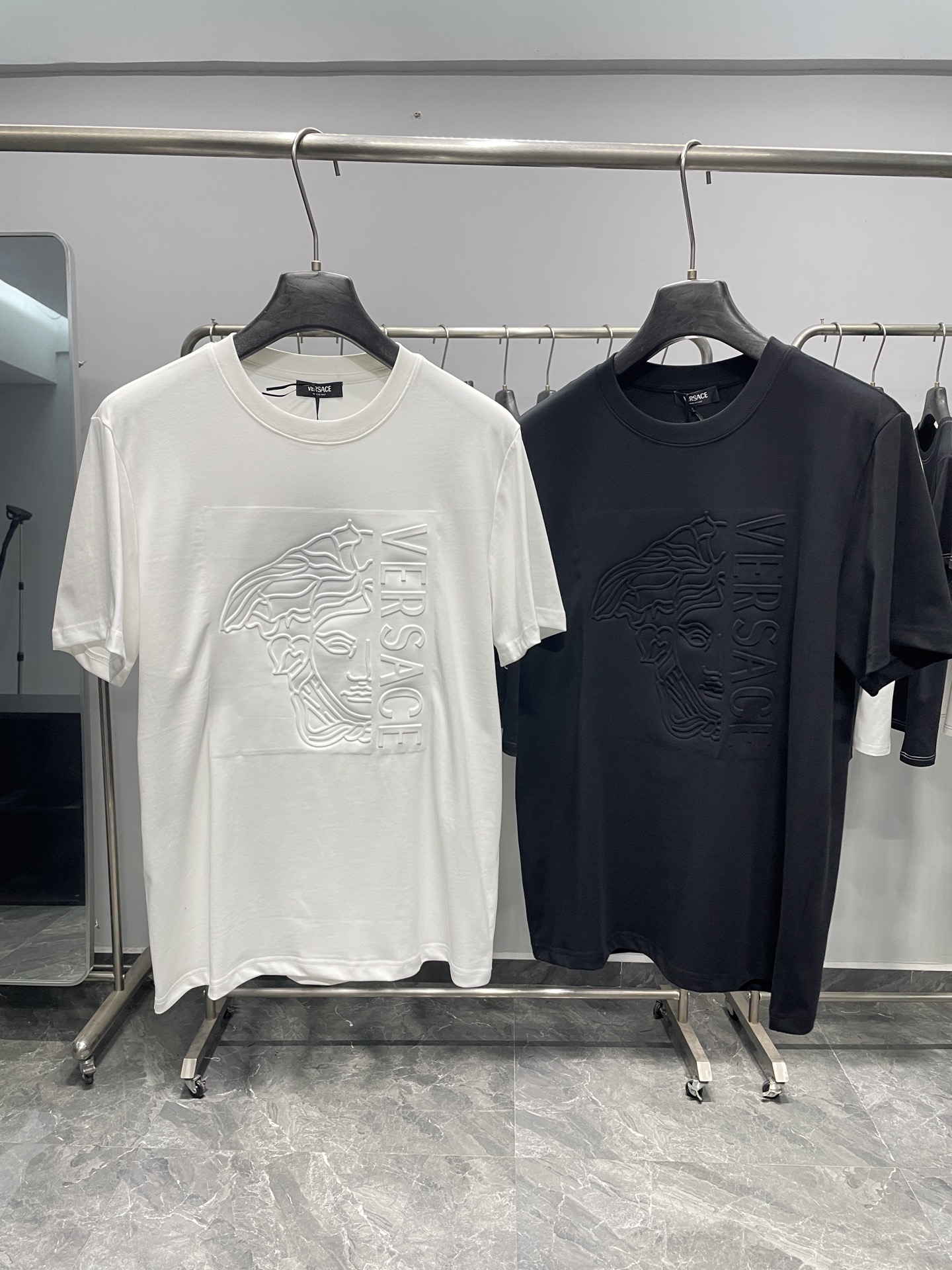 NO:857859,VER26SS new spring and summer three-dimensional relief embossed Medusa cotton round neck short-sleeved T-shirt!  Minimalist luxury, classic and timeless!  It is an essential wardrobe item that perfectly combines the brand's iconic aesthetics with everyday practicality.  The front uses a three-dimensional relief embossing process to present the classic Medusa head and vertical VER letters. It is low-key but highly recognizable. It injects the brand's luxury genes into the texture without unnecessary colors. It is available in black and white, whether it is pure white or deep black, it can adapt to different outfit moods and is a timeless style.  The basic luxury model of the moment. The high-count cotton fabric imported from Italy is selected, which is soft and skin-friendly, has excellent breathability and perspiration, and is not easy to deform after long-term wear. The delicate knitted texture and flat stitching technology, from the collar to the hem, highlight the exquisite workmanship of high-end ready-to-wear. The upper body has a full drape feeling, taking into account comfort and stiffness.  It is an excellent representative of 'low-key luxury'. It abandons exaggerated prints and uses embossed dark patterns to convey taste. It is not only suitable for smart occasions when commuting, but also can control the relaxed atmosphere of casual outings. It is the core item of light luxury and minimalist style. It can be paired with straight jeans and white shoes every day to create a refreshing and youthful look, and it is perfect for outdoor wear when commuting.  A simple suit paired with drapey trousers will give you a calm and elegant look. For street-style wear, you can layer metal necklaces with cargo shorts and dad shoes to easily unlock multiple advanced styles. This T-shirt carries the most profound brand heritage in the simplest form. It is a classic luxury basic style worth buying, allowing you to show your high-end taste in a low-key manner.  Color White, Black Size S-XXL Size Reference S Size Shoulder Width 43 Bust 100 Length 69 M Size Shoulder Width 44 Bust 104 Length 70 L Size Shoulder Width 45 Bust 108 Length 71 XL Size Shoulder Width 46 Bust 112 Length 72 2  suit,necklace,19860909VER26SS春夏新款立体浮雕压纹美杜莎纯棉圆领短袖T恤！ 极简奢感,经典永不过时！是将品牌标志性美学与日常实穿性完美融合的衣橱刚需单品. 正面以立体浮雕压纹工艺呈现经典美杜莎头像与垂直VER字母,低调却极具辨识度,无需多余色彩,便将品牌的奢华基因注入肌理之中.黑白两色可选,无论是纯净白还是深邃黑,都能适配不同穿搭情绪,是永不过时的奢品基础款.甄选意大利进口高支棉面料,触感柔软亲肤,透气排汗性优异,久穿不易变形.细腻的针织纹理与平整的车线工艺,从领口到下摆都彰显着高级成衣的精致做工,上身垂坠感十足,兼顾舒适与挺括感. 它是“低调奢华”的绝佳代表,摒弃了夸张印花,用压纹暗纹传递品味,既适合商务通勤的干练场合,也能驾驭休闲出街的松弛氛围,是轻奢风、极简风穿搭的核心单品.日常可搭配直筒牛仔裤与小白鞋打造清爽少年感,通勤时外搭极简西装、配垂感西裤尽显沉稳大气,街头风穿搭则可叠戴金属项链,搭配工装短裤与老爹鞋,轻松解锁多元高级造型.这件T恤用最简约的形式,承载了最厚重的品牌底蕴,是值得入手的经典奢品基础款,让你在低调中尽显高级品味. 颜色白色、黑色 尺码S-XXL 尺寸参考 S码肩宽43胸围100衣长69 M码肩宽44胸围104衣长70 L码肩宽45胸围108衣长71 XL码肩宽46胸围112衣长72 2XL码肩宽47胸围116衣长73,,shorts,jeans,T-shirt,tees，t-shirt,business suit,necklace,,Men's clothing