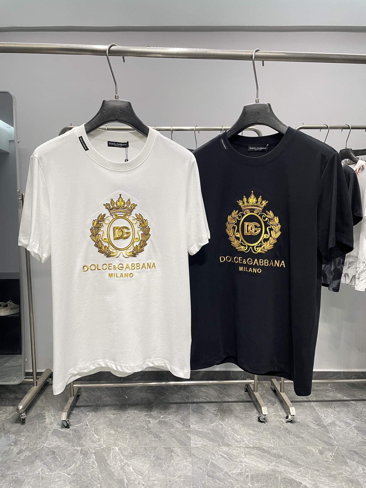 NO:857839,DG26SS new spring and summer crown embroidery pure cotton round neck short-sleeved T-shirt!  The daily expression of Italian elegance is the perfect fusion of Italian luxury and street casualness, with its own aristocratic aura yet still being practical and wearable.  The luxury brand originating from Milan turns the iconic crown and DG letter logo into heavy gold thread embroidery, paired with a surrounding laurel leaf pattern, shining brightly on a pure white or pure black base. It not only continues the brand's palace retro genes, but also adapts to the modern urban rhythm with neat tailoring. The double-label design on the neckline and the bottom  The wash water label on the display highlights the exquisite craftsmanship made in Italy. The pure cotton fabric is soft and skin-friendly, breathable and sweat-absorbent, and is both comfortable and crisp. Whether it is daily commuting or casual outings, it can maintain a refreshing and neat silhouette, and will not easily deform after long-term wear. It is a basic luxury product that can accompany you through many seasons.  The black gold/white gold color scheme brings a sense of luxury, and the simple round neck is not flattering on the body shape. It can be worn alone to highlight the embroidery details, or can be layered with suits and jackets, suitable for business and leisure, date parties and other scenarios. Pair the bottoms with trousers of the same brand to create an elegant Italian gentleman.  For a casual street style, paired with jeans or overalls, it is a timeless luxury basic in your wardrobe. This T-shirt is not only a piece of clothing, but also a low-key carrier of taste, allowing you to always feel the luxurious style from Milan in your daily life.  Color White, Black Size S-XXL Size Reference S Size Shoulder Width 43 Bust 100 Length 69 M Size Shoulder Width 44 Bust 104 Length 70 L Size Shoulder Width 45 Bust 108 Length 71 XL Size Shoulder Width 46 Bust 112 Length 72 2  suit,19860909DG26SS春夏新款皇冠刺绣纯棉圆领短袖T恤！ 意式奢雅的日常表达,是意式奢华与街头休闲的完美融合,自带贵族气场却不失实穿性. 源自米兰的奢侈品牌,将标志性的皇冠与DG字母徽标化作重工金线刺绣,搭配环绕的月桂叶纹样,在纯白或纯黑基底上熠熠生辉,既延续了品牌的宫廷复古基因,又以利落剪裁适配现代都市节奏.领口的双标设计与下摆的洗水标,处处彰显意大利制造的精致工艺.纯棉面料,触感柔软亲肤,透气吸汗,兼顾舒适与挺括.无论是日常通勤还是休闲出街,都能保持清爽利落的版型,久穿不易变形,是能陪伴你度过多个季节的基础款奢品. 黑金/白金的配色自带高级感,简约圆领不挑身形,既能单穿凸显刺绣细节,也可作为内搭叠穿西装、夹克,适配商务休闲、约会聚会等多种场景.下装搭配同品牌西裤可打造优雅意式绅士风,搭配牛仔裤或工装裤则能解锁随性街头感,是衣橱里永不过时的奢品基础款.这件T恤不止是一件衣物,更是低调彰显品味的载体,让你在日常中也能时刻感受来自米兰的奢雅格调. 颜色白色、黑色 尺码S-XXL 尺寸参考 S码肩宽43胸围100衣长69 M码肩宽44胸围104衣长70 L码肩宽45胸围108衣长71 XL码肩宽46胸围112衣长72 2XL码肩宽47胸围116衣长73,,jeans,jackets & coats,T-shirt,tees，t-shirt,business suit,,Men's clothing