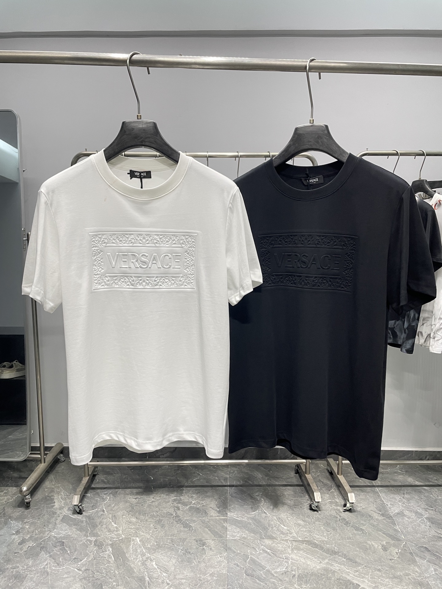 NO:857861,VER26SD spring and summer new three-dimensional relief embossed letter pattern pure cotton round neck short-sleeved T-shirt!  A low-key and elegant daily choice, based on pure cotton fabric, it perfectly blends Italian luxury and comfortable wear. It is a versatile core item in the wardrobe of urban elites.  Looking at the details, the iconic three-dimensional embossed LOGO on the chest is the visual focus. The same color relief technology makes the letters and the baroque curly grass pattern border clear, which not only retains the brand recognition, but also avoids exaggeration and publicity, and reveals a sense of sophistication in a low-key manner. The round neckline is edged with fine ribs, with neat and solid routing, which is not easily deformed after long-term wear, and fits the neck line without being tight, taking into account both comfort and style.  Stiffness. The selected high-quality cotton brings a skin-friendly and breathable wearing experience with excellent moisture absorption and perspiration performance. Whether it is daily commuting or leisure travel in spring and summer, you can stay fresh and comfortable. The classic black and white two-color selection is suitable for diverse styles. The white model is clean and neat, with a youthful and refreshing temperament; the black model is calm and restrained, more mature, and can easily meet the dressing needs of different occasions.  In terms of matching, its highly malleable bottoms can be paired with trousers or straight jeans of the same brand to create a smart business sense; it can also be layered with denim jackets and casual jackets to unlock casual street style; paired with sports shorts, it can switch to a relaxed vacation mode. Whether worn alone or as an inner layer, it can easily highlight the taste and style of the wearer. It is a light luxury basic style that can run through the four seasons and adapt to various life scenes. Color White, Black Size S-XXL Size Reference  S size shoulder width 43 bust 100 length 69 M size shoulder width 44 bust 104 length 70 L size shoulder width 45 bust 108 length 71 XL size shoulder width 46 bust 112 length 72 219860909VER26SD春夏新款立体浮雕压纹字母图案纯棉圆领短袖T恤！ 低调奢雅的日常之选,以纯棉面料为基底,将意式奢华与舒适穿着感完美融合,是都市精英衣橱里的百搭核心单品. 从细节来看,胸前标志性的立体压纹LOGO是视觉焦点同色系浮雕工艺让字母与巴洛克卷草纹边框层次分明,既保留了品牌辨识度,又避免了夸张张扬,低调中透着精致感.圆领领口采用细密罗纹包边,走线工整扎实,久穿不易变形,贴合颈部线条却不紧绷,兼顾舒适与版型挺括度.精选的优质棉带来亲肤透气的穿着体验,吸湿排汗性能优异,无论是春夏日常通勤还是休闲出行,都能保持清爽自在.经典的黑白双色选择,适配多元风格场景白色款干净利落,自带少年感与清爽气质；黑色款沉稳内敛,更显成熟大气,轻松满足不同场合的穿搭需求. 在搭配上,它的可塑性极强下装可搭配同品牌西裤或直筒牛仔裤,打造干练商务感；也可叠穿牛仔外套、休闲夹克,解锁随性街头风；搭配运动短裤则能切换松弛度假模式.无论是单穿还是作为内搭,都能轻松凸显穿着者的品味与格调,是一件能贯穿四季、适配各种生活场景的轻奢基础款. 颜色白色、黑色 尺码S-XXL 尺寸参考 S码肩宽43胸围100衣长69 M码肩宽44胸围104衣长70 L码肩宽45胸围108衣长71 XL码肩宽46胸围112衣长72 2XL码肩宽47胸围116衣长73,,shorts,jeans,jackets & coats,jackets & coats,T-shirt,tees，t-shirt,,Men's clothing