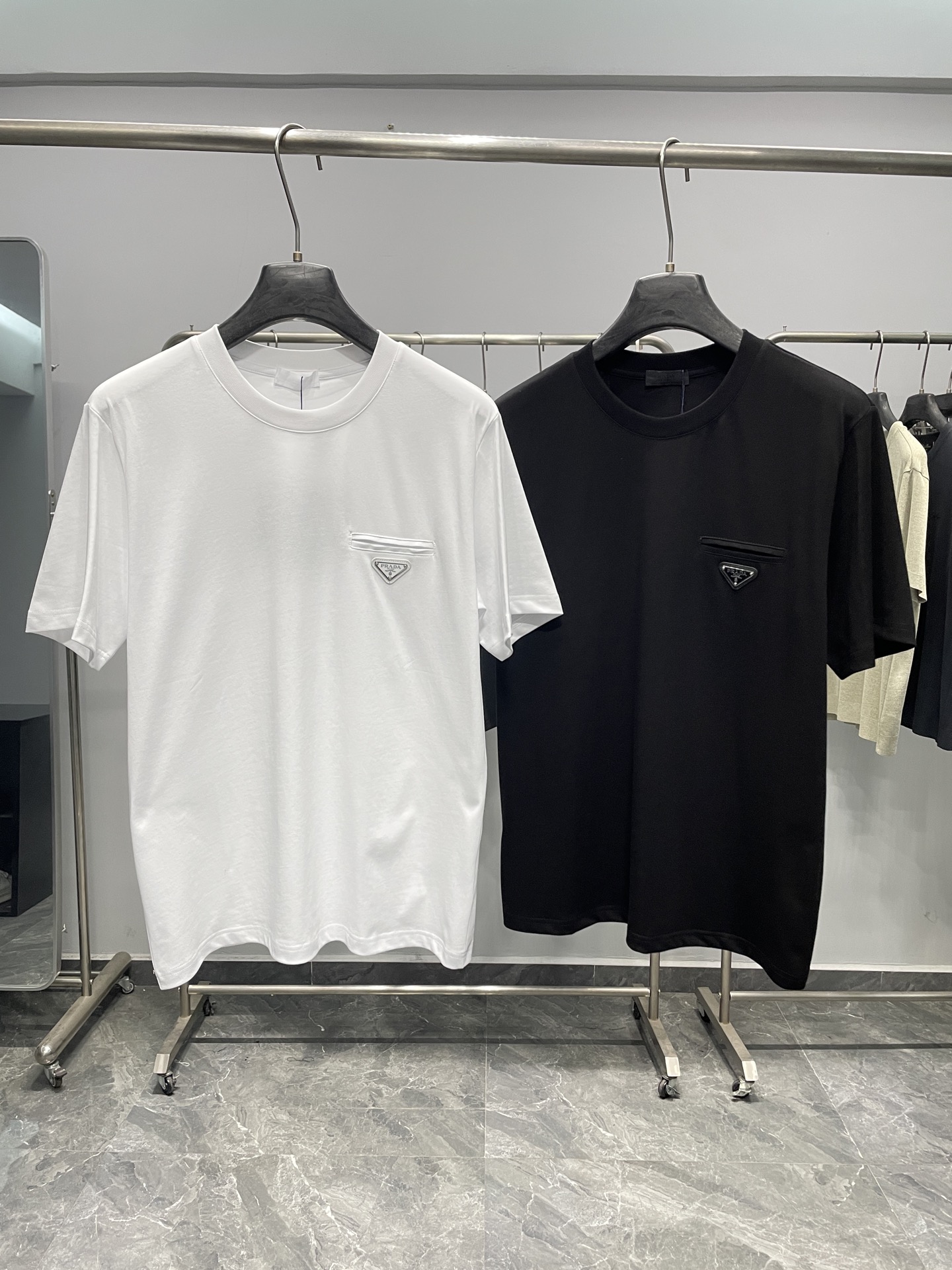 NO:777718,PRA26SS new spring and summer new plain knitted cotton basic round neck short Tee, the same style for men and women with triangular logo fake pockets casual pullover short-sleeved T-shirt!  Trading company channels are rare and available on the official website simultaneously!  P's new T-shirt has won widespread praise for its exquisite fabrics, clever design and comfortable fit!  It is not only a worthy item for daily matching, but also an indispensable choice to show your personal taste and style!  This short T-shirt is made of custom-woven and dyed plain-knit cotton. It feels soft and porcelain, and has good overall breathability and moisture absorption!  In terms of accessories, the ribbed round neck stitching design is dyed in the same vat, which is durable in washing and not easy to deform!  The fake pocket on the chest is combined with the brand triangle badge, which is embellished on the clothes. It is eye-catching and can be called the finishing touch!  This T-shirt is cut in a basic straight silhouette, which can be easily worn by both men and women. Whether paired with casual pants or trousers, it can show a sense of fashion and taste!  Not only that, the comfortable wearing experience also highlights the elegance and relaxed atmosphere!  Color White, Black Size S-XXL Size Reference S Size Shoulder Width 45 Bust Length 67 M Size Shoulder Width 46 Bust 104 Length 68 L Size Shoulder Width 47 Bust Length 69 XL Size Shoulder Width 48 Bust 112 Length 70 219860909PRA26SS春夏新款平纹针织棉布基础圆领短Tee,男女同款三角标假口袋休闲套头短袖T恤衫！贸易公司渠道稀出,同步官网发售！P家新款T恤以其精湛的面料、巧妙的设计和舒适的版型赢得了广泛好评！它不仅是日常搭配中值得拥有的单品,更是展现个人品味和风格的不可或缺之选！ 该短Tee采用定织定染平纹针织棉布制成,手感瓷实柔软,整体透气吸湿性佳！辅料方面,同缸色染罗纹圆领拼接设计,经久耐洗不易变形！胸前的假口袋与品牌三角标徽章相结合,点缀在衣服上,醒目吸睛,堪称点睛之笔的存在！这款T恤采用基础直筒版型剪裁,男女都能轻松驾驭,无论是搭配休闲裤还是西裤,都能展现出时尚感和品味！不仅如此,在舒适的穿着体验下也凸显出优雅与轻松的氛围！ 颜色白色、黑色 尺码S-XXL 尺寸参考 S码肩宽45胸围衣长67 M码肩宽46胸围104衣长68 L码肩宽47胸围衣长69 XL码肩宽48胸围112衣长70 2XL码肩宽49胸围116衣长71,,prada,T-shirt,tees，t-shirt,,Men's clothing