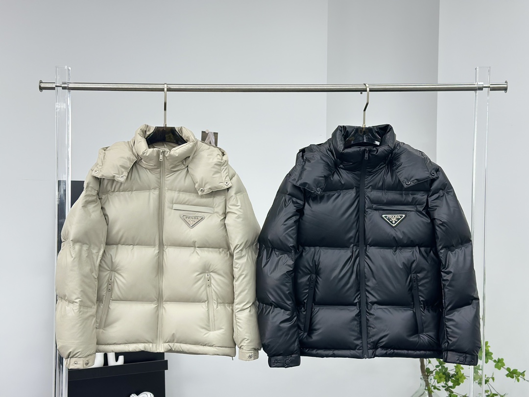 Prada 普拉达黑科技压胶羽绒服

秋冬新款高密度哑光漆面尼龙羽绒夹克，男女同款金属三角大标口袋可拆卸连帽立领羽绒服外套!贸易公司渠道稀出，同步官网发售!
P家新款羽绒服在保暖性能和时尚设计之间取得了完美平衡，并且成为2024年秋冬季街头潮流中的亮点!

它采用了精选客供进口高密度哑光漆面尼龙材质，让面料表面纹理细腻清晰，呈现出肉眼可见的高级质感!不仅如此这款外套还具备防风、防水、耐磨和防撕裂等功能性，超级出色!在内里方面，采用了高含量欧标羽绒，并结合横向绗缝工艺进行分格填充，使得整体保暖蓬松且不显臃肿感!胸前口袋上的硕大三角标金属徽章装饰简约大气，将奢华身份展露无遗!这款外套还特别定制了刻有品牌字样的哑光漆面金属拉链，并经过全压胶处理，品相细节无法挑剔，设计上采用可拆卸式连帽立领造型，搭配基础直筒版型剪裁，上身既保暖又不挑风格与造型!男女同款推荐，不失任何年龄阶段的限制，在时尚圈引起一番热议!