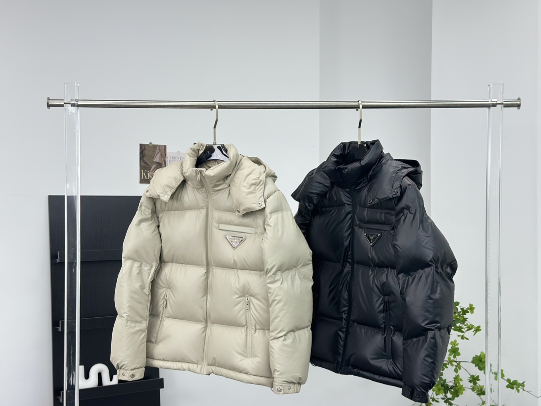 Prada 普拉达黑科技压胶羽绒服

秋冬新款高密度哑光漆面尼龙羽绒夹克，男女同款金属三角大标口袋可拆卸连帽立领羽绒服外套!贸易公司渠道稀出，同步官网发售!
P家新款羽绒服在保暖性能和时尚设计之间取得了完美平衡，并且成为2024年秋冬季街头潮流中的亮点!

它采用了精选客供进口高密度哑光漆面尼龙材质，让面料表面纹理细腻清晰，呈现出肉眼可见的高级质感!不仅如此这款外套还具备防风、防水、耐磨和防撕裂等功能性，超级出色!在内里方面，采用了高含量欧标羽绒，并结合横向绗缝工艺进行分格填充，使得整体保暖蓬松且不显臃肿感!胸前口袋上的硕大三角标金属徽章装饰简约大气，将奢华身份展露无遗!这款外套还特别定制了刻有品牌字样的哑光漆面金属拉链，并经过全压胶处理，品相细节无法挑剔，设计上采用可拆卸式连帽立领造型，搭配基础直筒版型剪裁，上身既保暖又不挑风格与造型!男女同款推荐，不失任何年龄阶段的限制，在时尚圈引起一番热议!