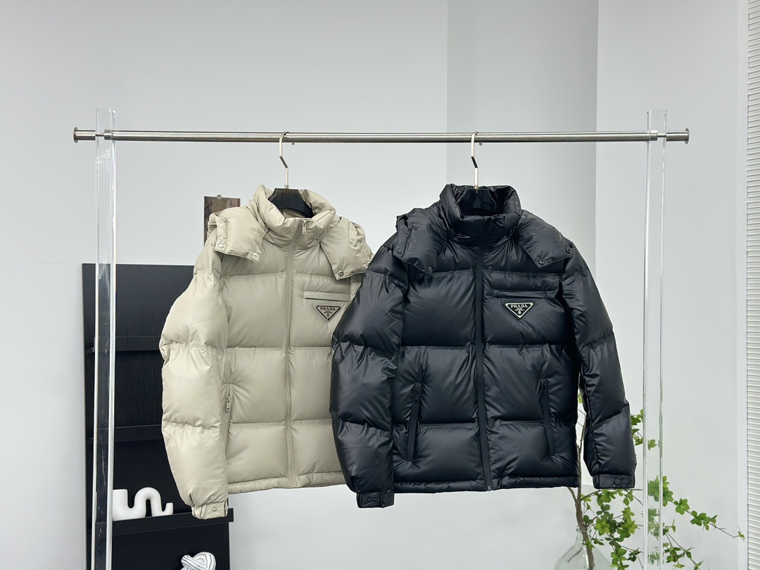 Prada 普拉达黑科技压胶羽绒服

秋冬新款高密度哑光漆面尼龙羽绒夹克，男女同款金属三角大标口袋可拆卸连帽立领羽绒服外套!贸易公司渠道稀出，同步官网发售!
P家新款羽绒服在保暖性能和时尚设计之间取得了完美平衡，并且成为2024年秋冬季街头潮流中的亮点!

它采用了精选客供进口高密度哑光漆面尼龙材质，让面料表面纹理细腻清晰，呈现出肉眼可见的高级质感!不仅如此这款外套还具备防风、防水、耐磨和防撕裂等功能性，超级出色!在内里方面，采用了高含量欧标羽绒，并结合横向绗缝工艺进行分格填充，使得整体保暖蓬松且不显臃肿感!胸前口袋上的硕大三角标金属徽章装饰简约大气，将奢华身份展露无遗!这款外套还特别定制了刻有品牌字样的哑光漆面金属拉链，并经过全压胶处理，品相细节无法挑剔，设计上采用可拆卸式连帽立领造型，搭配基础直筒版型剪裁，上身既保暖又不挑风格与造型!男女同款推荐，不失任何年龄阶段的限制，在时尚圈引起一番热议!