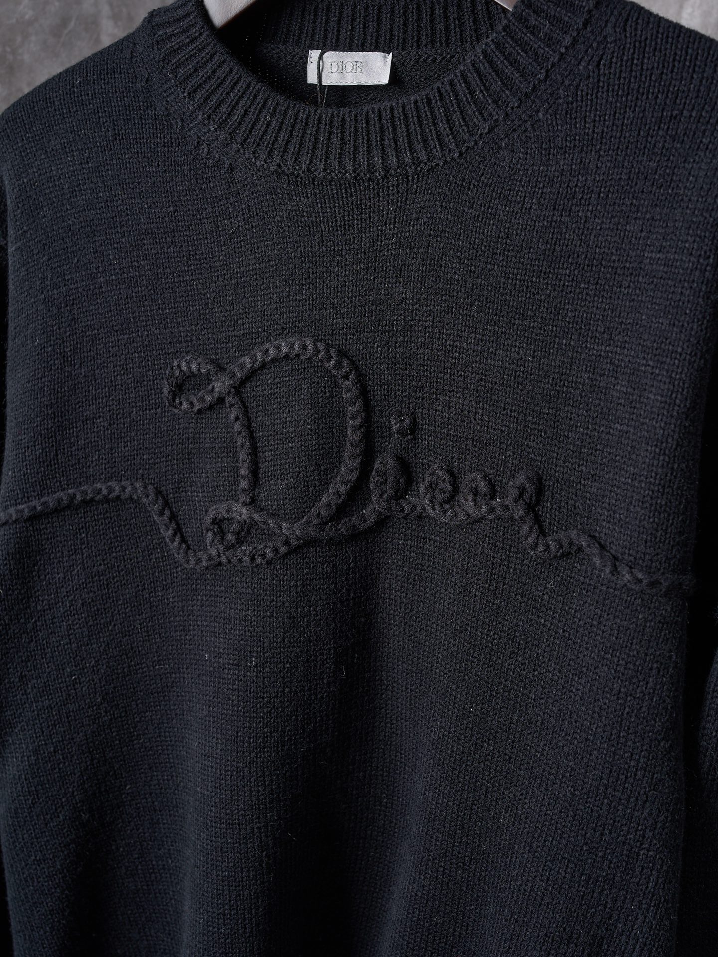 P225


【实物挂拍】DIOR/迪奥 机缝线绣标识针织圆领长袖毛衣


【颜色】黑色 杏色
【现货】S M L XL

这款针织衫是二零二六春季男装系列新品，饰以Dior Ribbon 标志，向Dior 工坊的精湛工艺致敬。采用白色绵羊毛平纹针织面料精心制作，搭配罗纹圆领、袖口和底边。优雅版型，可与牛仔裤搭配，打造休闲时髦的精致造型。
Dior Ribbon 刺绣，罗纹圆领、袖口和底边

采用50%羊毛，50%棉纱。
胸口徽标采用正7针进口机织出，大小尺寸按原版1：1数据定织。
成衣洗水-去除羊毛表面杂质-固色-固定版型-添加手感。