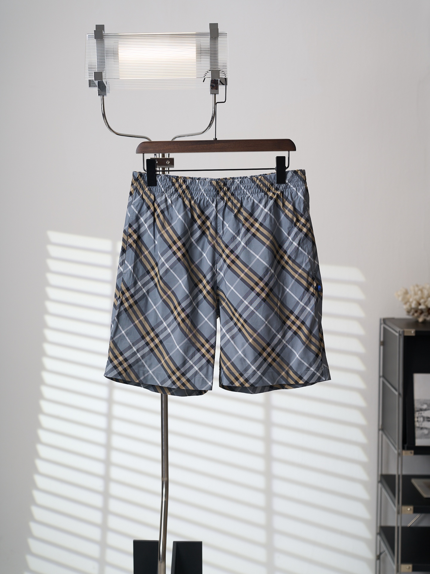 NO:931773,[Real object hanging] BURBERRY/Burberry blue and gray twill plaid shorts [Ready stock] S M L  Built-in polyester fiber technical mesh lining, the hollow mesh structure greatly improves air circulation efficiency, accelerates sweat evaporation, and keeps the body feeling refreshed during exercise. Checking technology High-standard checking technology is adopted, and every step from the cutting bed to the sewing machine is precisely controlled. The sewing master is required to restore every checkered line from the waist, placket to trousers, and the crisscrossing patterns are tightly stitched at the seams.  It bites like a precision gear, avoiding the dislocation of the plaid and making it look awkward at first glance. Sewing details: The waistband is designed with multiple elastic threads, which has good elasticity and tolerance, is easy to put on and take off, and can also improve the fit of the waist. The drawstring design is retained at the front waist, and the edges of the drawstring eyelets are densely packed with circular lock stitches to completely wrap the fabric incisions, forming a strong 'ring-shaped protective layer' that can withstand repeated pulling without stripping or cracking.  The side pockets adopt a diagonal pocket structure, with tacks on both sides of the pocket, and smooth stitching to enhance the firmness of the pocket. The sides of the trousers are embellished with small woven marks and a blue embroidered logo on a black background, which increases the sense of detail and recognition. The back panel is equipped with a single-sided patch pocket, and the bag flap and the trousers body plaid are naturally connected. At the same time, the snap buttons can be hidden to increase the beauty and make the back less monotonous.,,burberry,burberry,shorts,19860909【实物挂拍】BURBERRY/巴宝莉 蓝灰斜纹格短裤【现货】S M L XL 面料选择 选用轻薄尼龙梭织格纹面料,布面纤维排列紧密,抗皱性较强的同时不失轻便,透气性强等特点.格纹由灰色、卡其等多色粗线条交织而成,层次感比较强,既有休闲感,也能提升辨识度. 网眼内衬 内置聚酯纤维科技织网衬里,镂空网眼结构大幅提升空气流通效率,能加速汗液蒸发,运动时也能保持体感清爽. 对格工艺 采用高标准对格工艺,从裁床到缝纫机每一处都精准把控.要求缝纫师从腰头、门襟到裤身,每一处格纹线条还原,纵横交错的纹路在接缝处严丝合缝, 如精密齿轮般咬合,避免了格纹错位杂乱而一眼尬. 缝纫细节 腰头采用多道松紧车线设计,弹力包容性好,穿脱方便,也能提升腰部贴合度.前腰位置保留抽绳设计,抽绳孔眼边缘采用密集的环形锁缝,将面料切口完全包裹,形成一个坚固的“环状保护层”,能承受反复拉扯而不脱线、不开裂. 侧边口袋采用斜插袋结构,袋口两边均做套结,车线平整,强化口袋牢固度.裤身侧边带有小织唛点缀,黑底蓝色刺绣标识,增加细节感和辨识度. 后片设有单边贴袋,袋盖和裤身格纹衔接自然,同时能隐藏按扣增加美观性,也让背面不显单调.,,burberry,burberry,shorts,,Men's clothing