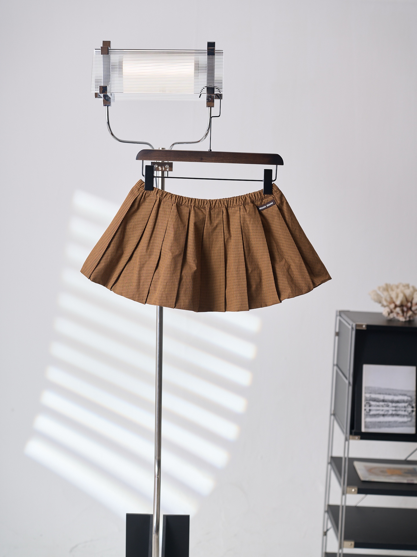 NO:936742,[Real auction] MiuMiu/Miu Miu retro brown logo plaid pleated miniskirt [Ready stock] 38 40 42 Customized retro brown tone denim fine plaid satin, draped and stiff, comfortable and close to the skin. Caramel chestnut brown lays the retro base, and the fine yarn-dyed plaid pattern smudges the gentle texture, blending the warmth of the autumn sycamore into the fabric into the skirt.  The iconic MiuMiu label is low-key embellishment on the side, adding a low-key sense of luxury. With the classic and chic Vichy fine plaid as the design skeleton, the pleats naturally drape along the brown texture and swell into a bud silhouette, creating ripples of texture when you walk; the hip and leg lines are cleverly optimized to create a gold A-line shape that is narrow at the top and wide at the bottom. The neat lines are wrapped in a gentle girlish feeling, overflowing with a retro relaxed style. 1.  Special machine positioning adopts imported special machine infrared positioning 'MiuMiu label' to make the position more precise and firm. 2. CNC high-temperature integrated pleating relies on constant temperature stamping of high-precision molds to lock the fiber texture, insert the entire flat fabric into the mold, and synchronously press at constant temperature and high pressure, relying on heat to fuse the fiber structure of the fabric, allowing the pleat grooves and pleat surfaces to permanently form a physical memory, and pressing out all the pleats on the entire piece of fabric at the same time. 3. The accordion pleat waist binding strips are shaped  The special binding strips for the waist are wrapped and closed by professional pulling equipment. The cloth edges are wrapped tightly and plumply, and are integrated with the elastic structure. The elastic stretch of the waistband is even, slim fit, miumiu, skirts, gold,19860909【实物挂拍】MiuMiu/缪缪 复古棕徽标格纹百褶超短裙【现货】38 40 42 定制复古棕调缇织细格贡缎,垂坠挺括,舒适贴肤.焦糖栗棕铺陈复古基底,细密色织格纹晕染温柔肌理,把秋日梧桐落进面料里的暖调揉进裙身. 标志性MiuMiu标签低调点缀侧边,增添了一份低调的奢华感.以经典别致的Vichy维希细格纹为设计骨架,百褶顺着棕调肌理自然垂坠膨起成花苞廓形,走路时漾开层层涟漪质感；巧妙优化胯部与腿部线条,打造上窄下宽的黄金A字版型.利落线条里裹着温柔少女感,漫溢复古松弛格调. 1. 专机定位 采用进口专机红外线定位“MiuMiu标签” 位置更为精准、牢固结实. 2. 数控高温一体压褶 依托高精度模具恒温冲压锁死纤维肌理,将整张平铺面料嵌入模具,通过恒温高压同步压制,依靠热力融合面料纤维结构,让褶沟、褶面永久形成物理记忆,一整片布同时压出全部褶裥. 3.风琴褶束腰捆条定型 腰位专用捆条经专业拉筒设备一体包合收边,布边包裹紧实饱满,结合松紧结构一体成型,腰头弹力伸缩均匀,修身版型,,miumiu,skirts,gold,,Men's clothing