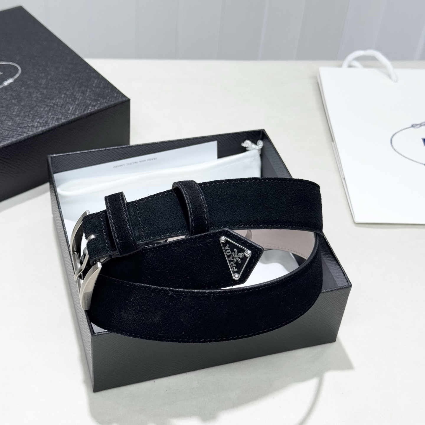 。 男女通用，P rada这款华美的绒面皮革腰带释放简约而精致的优雅气息 尖部的涂珐琅金属三角形徽标展现