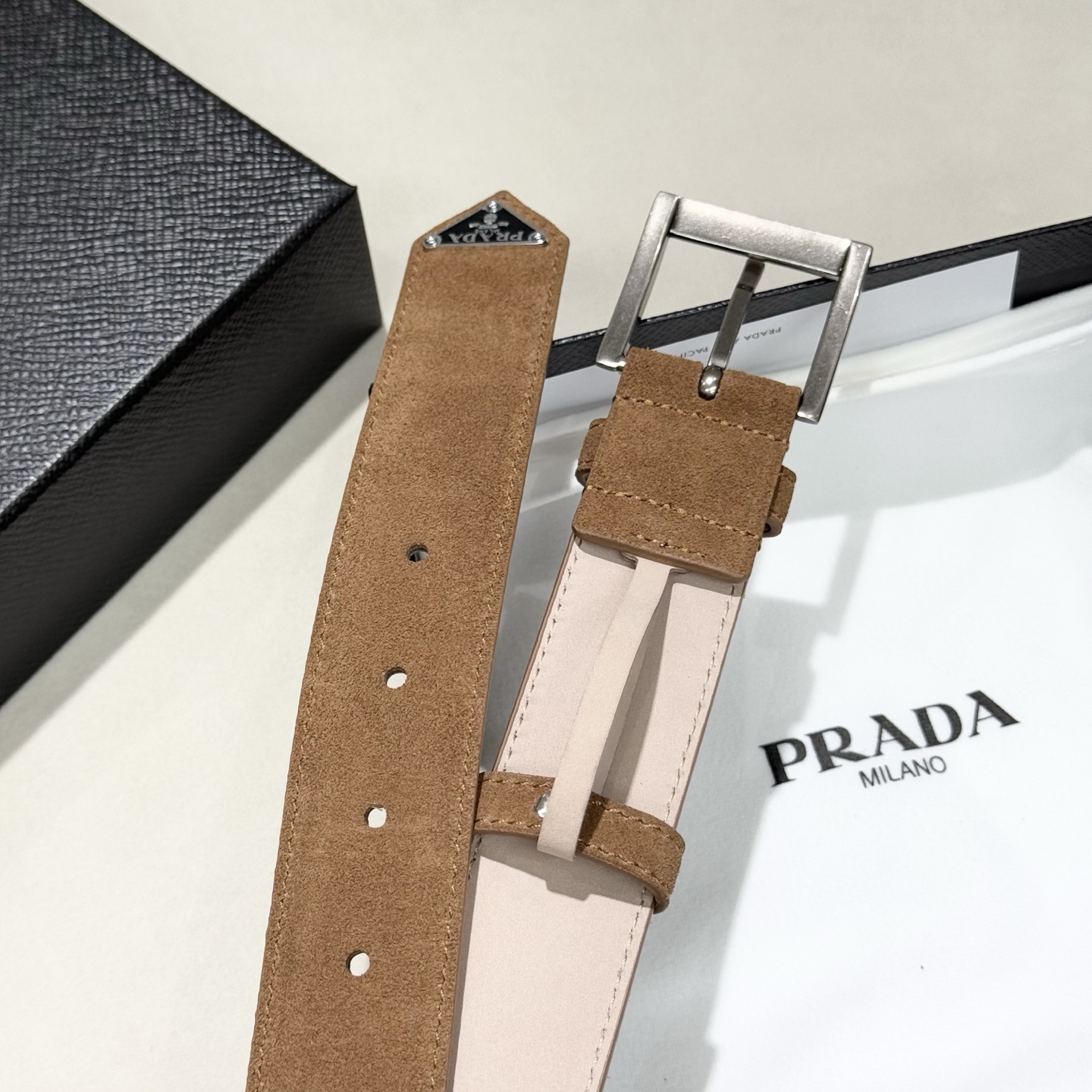。 男女通用，P rada这款华美的绒面皮革腰带释放简约而精致的优雅气息 尖部的涂珐琅金属三角形徽标展现