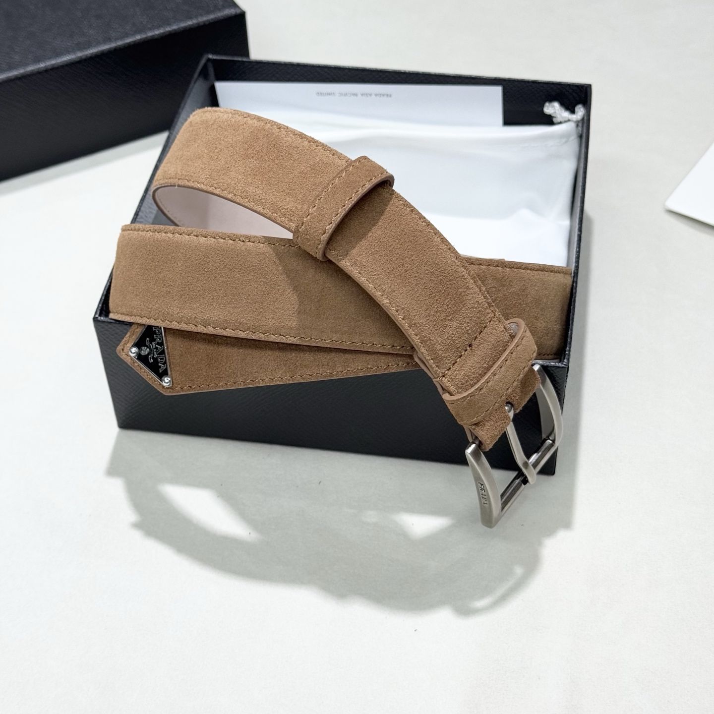 。 男女通用，P rada这款华美的绒面皮革腰带释放简约而精致的优雅气息 尖部的涂珐琅金属三角形徽标展现