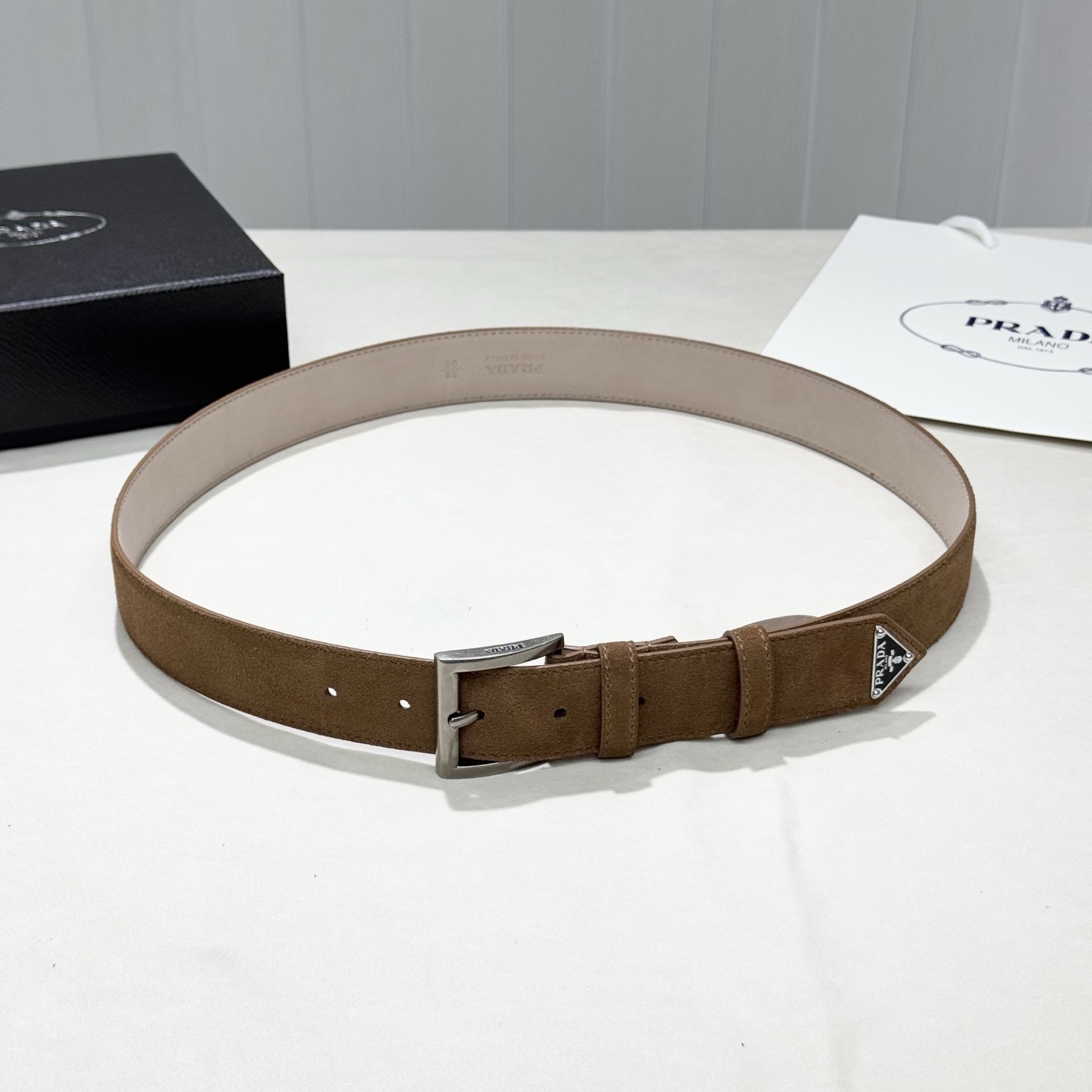 。 男女通用，P rada这款华美的绒面皮革腰带释放简约而精致的优雅气息 尖部的涂珐琅金属三角形徽标展现