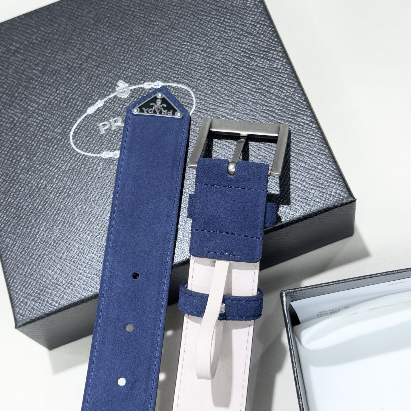 。 男女通用，P rada这款华美的绒面皮革腰带释放简约而精致的优雅气息 尖部的涂珐琅金属三角形徽标展现