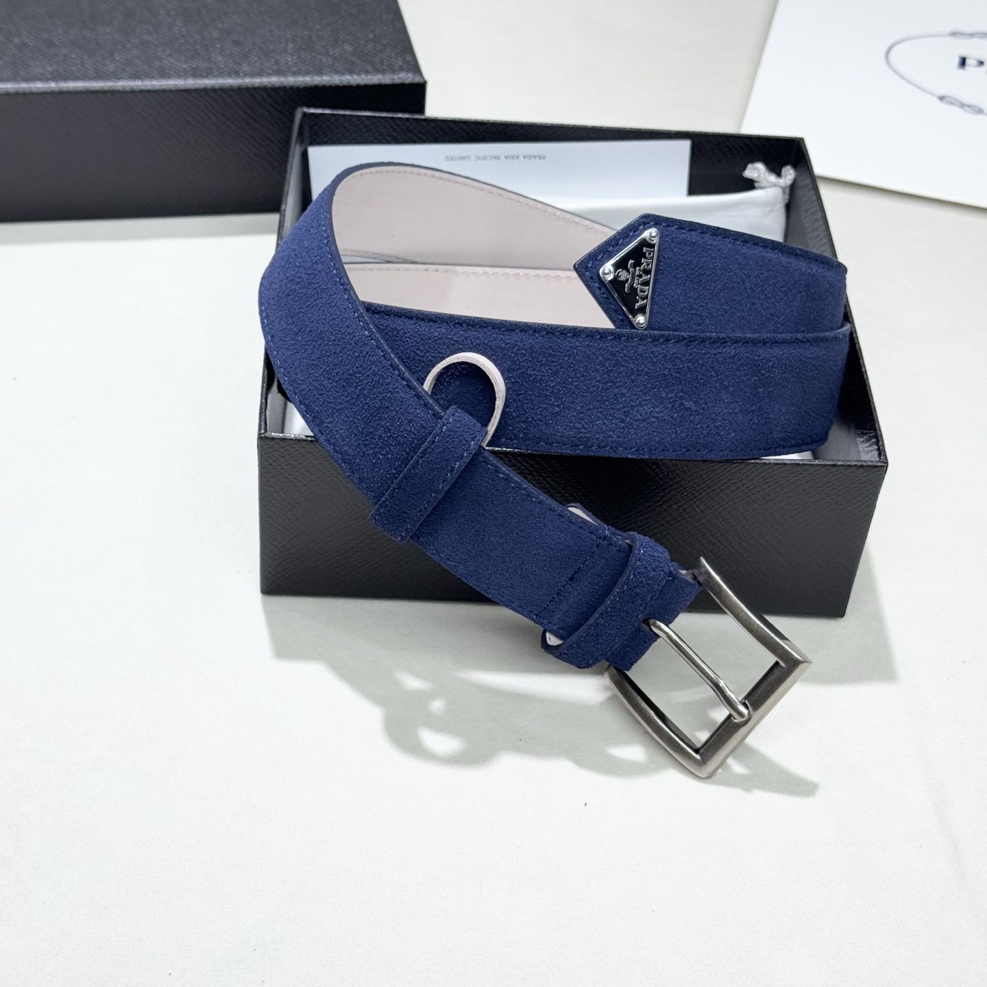 。 男女通用，P rada这款华美的绒面皮革腰带释放简约而精致的优雅气息 尖部的涂珐琅金属三角形徽标展现