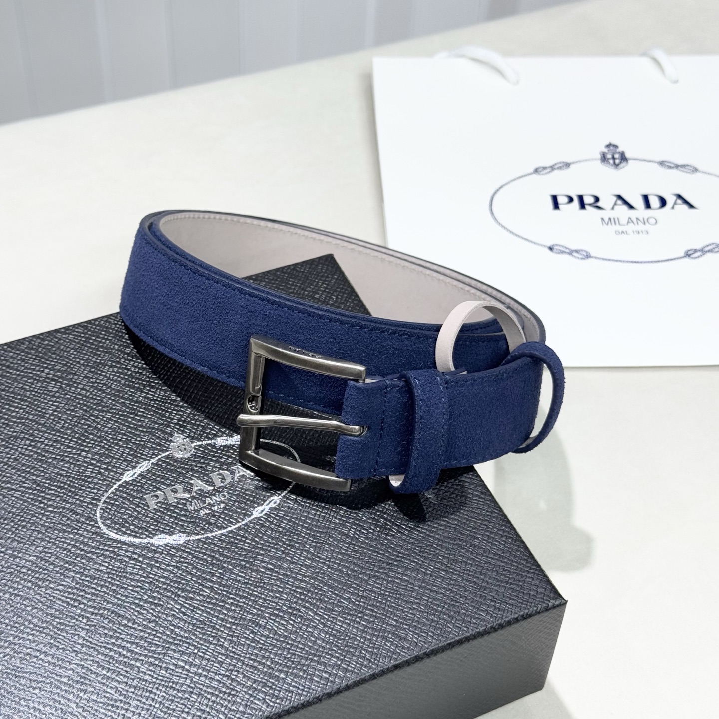 。 男女通用，P rada这款华美的绒面皮革腰带释放简约而精致的优雅气息 尖部的涂珐琅金属三角形徽标展现