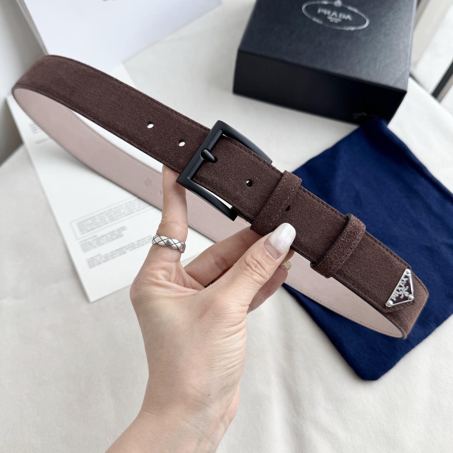 。 男女通用，P rada这款华美的绒面皮革腰带释放简约而精致的优雅气息 尖部的涂珐琅金属三角形徽标展现