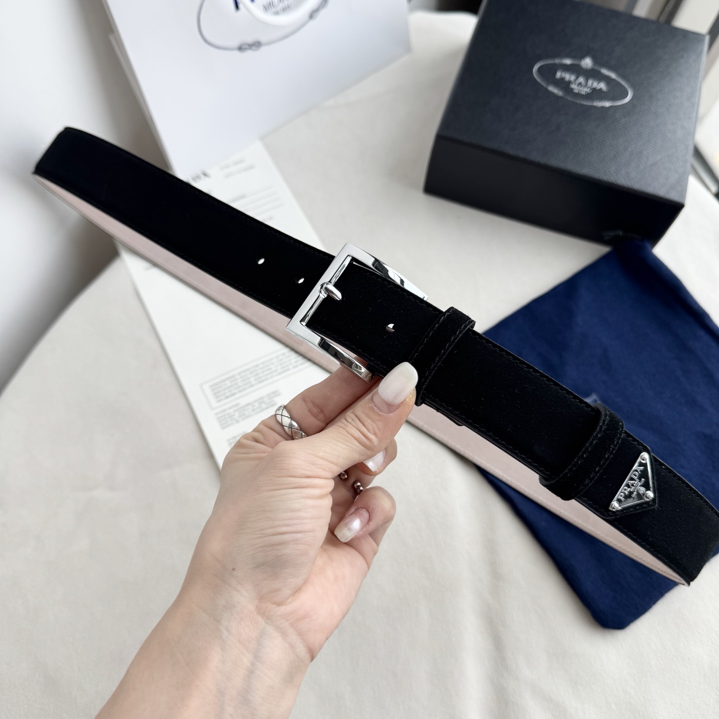 。 男女通用，P rada这款华美的绒面皮革腰带释放简约而精致的优雅气息 尖部的涂珐琅金属三角形徽标展现