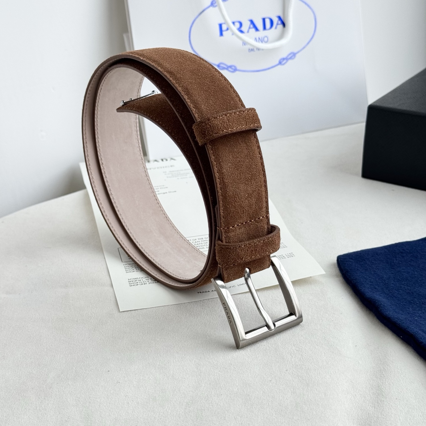 。 男女通用，P rada这款华美的绒面皮革腰带释放简约而精致的优雅气息 尖部的涂珐琅金属三角形徽标展现