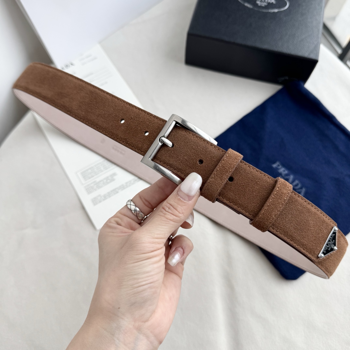 。 男女通用，P rada这款华美的绒面皮革腰带释放简约而精致的优雅气息 尖部的涂珐琅金属三角形徽标展现