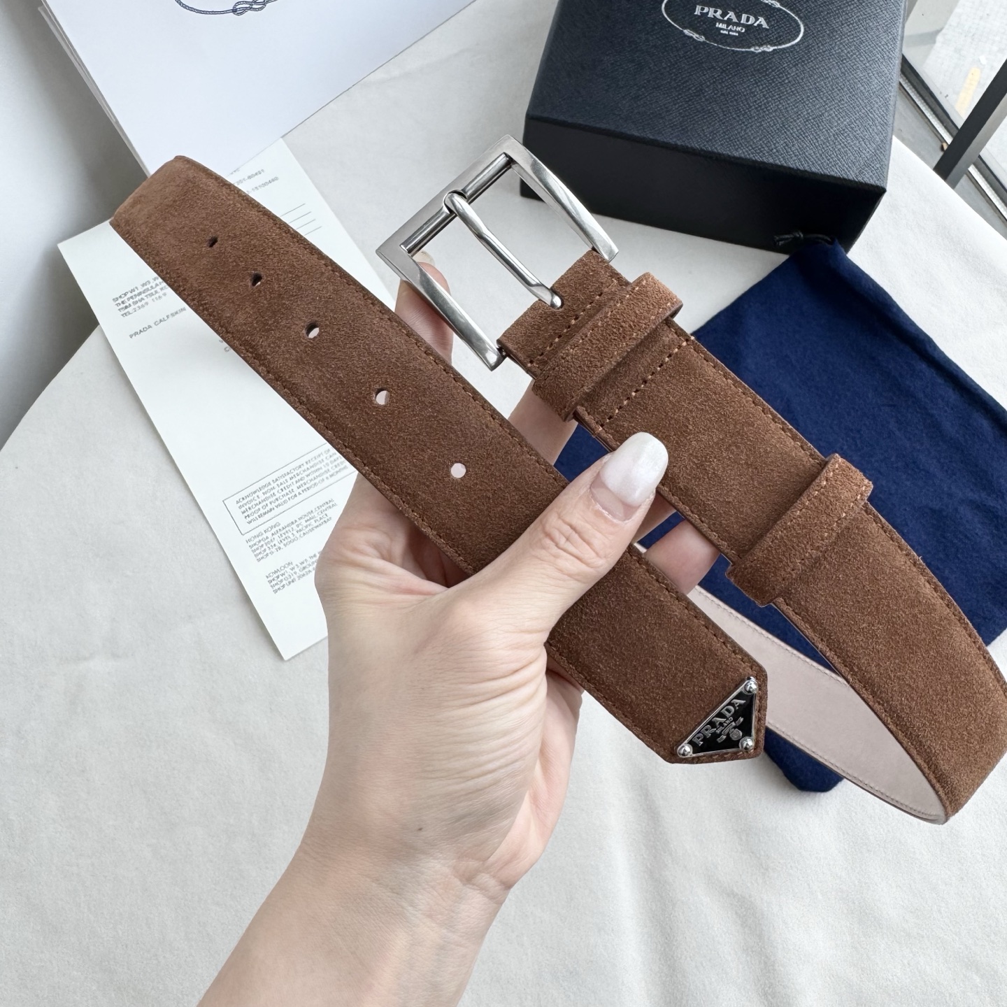 。 男女通用，P rada这款华美的绒面皮革腰带释放简约而精致的优雅气息 尖部的涂珐琅金属三角形徽标展现