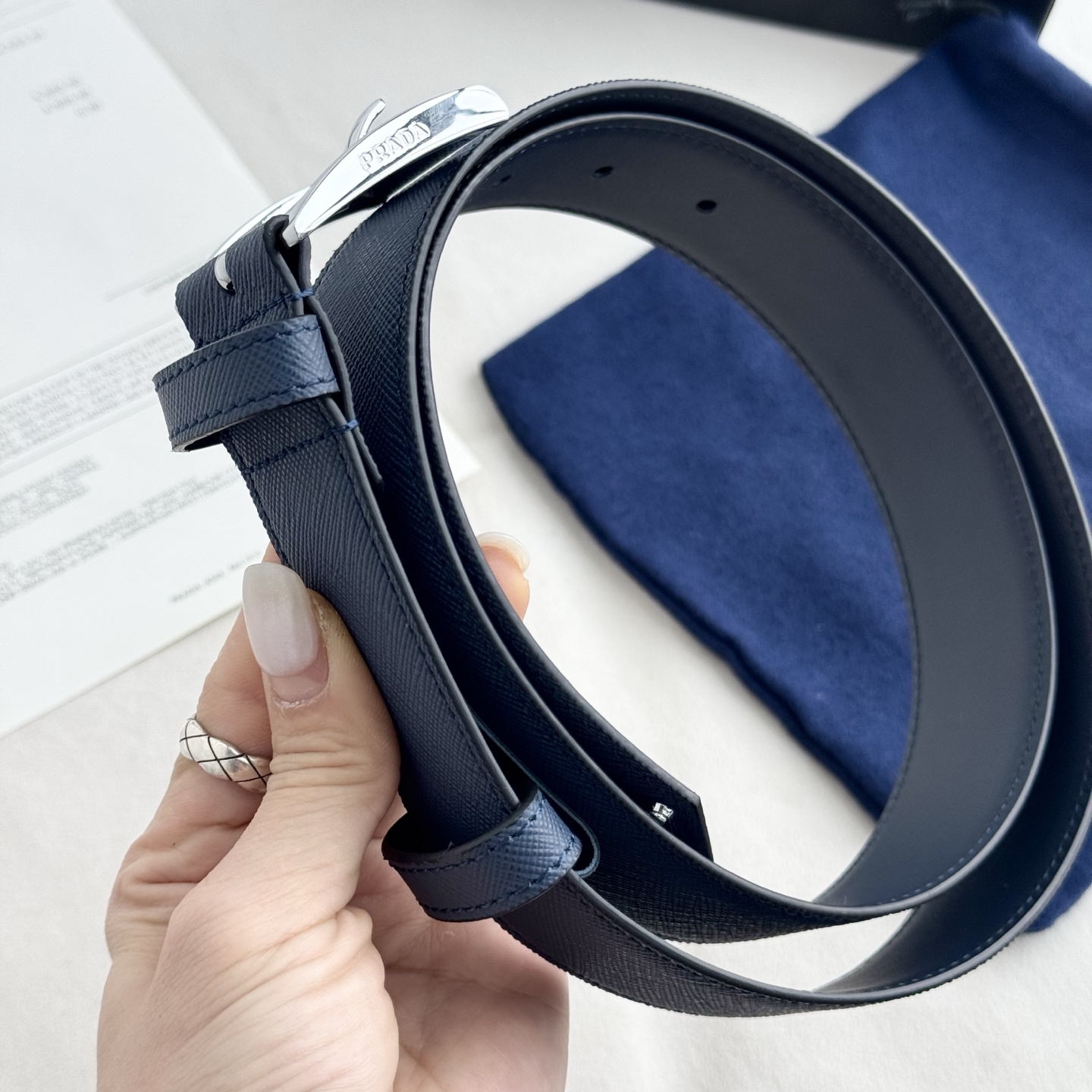 。 男女通用，P rada这款华美的十字纹牛皮腰带释放简约而精致的优雅气息 尖部的涂珐琅金属三角形徽标展