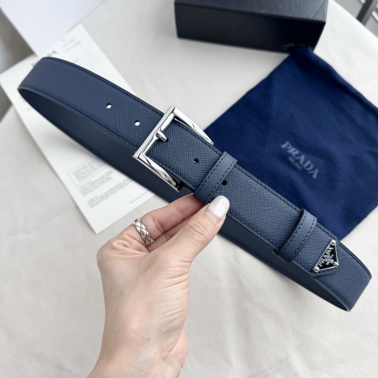 。 男女通用，P rada这款华美的十字纹牛皮腰带释放简约而精致的优雅气息 尖部的涂珐琅金属三角形徽标展