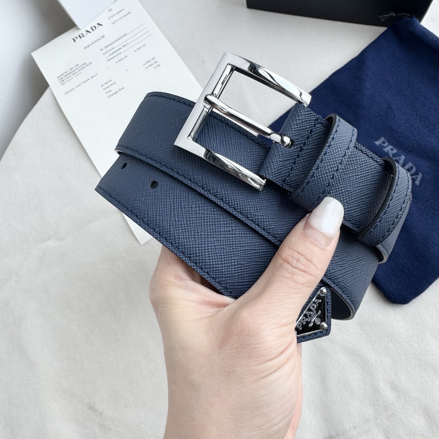 。 男女通用，P rada这款华美的十字纹牛皮腰带释放简约而精致的优雅气息 尖部的涂珐琅金属三角形徽标展