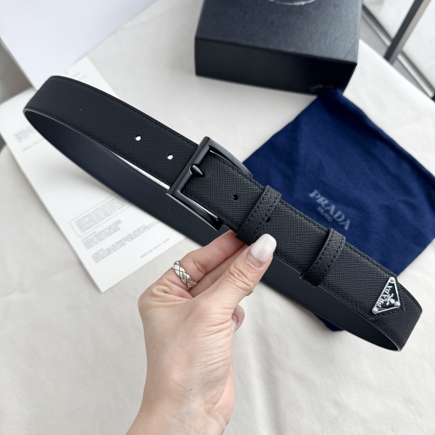 。 男女通用，P rada这款华美的十字纹牛皮腰带释放简约而精致的优雅气息 尖部的涂珐琅金属三角形徽标展