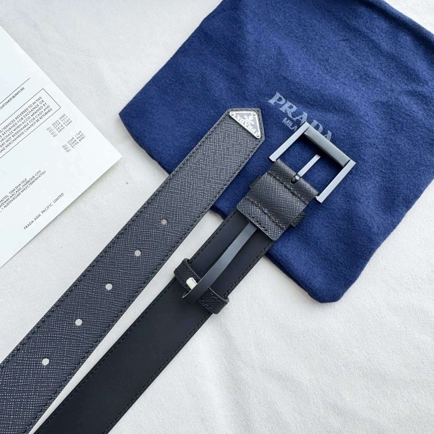 。 男女通用，P rada这款华美的十字纹牛皮腰带释放简约而精致的优雅气息 尖部的涂珐琅金属三角形徽标展