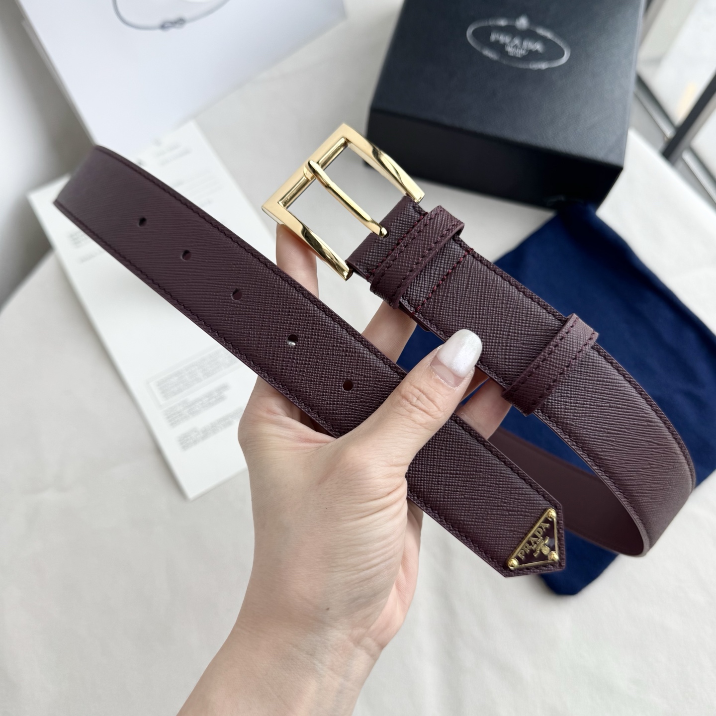 。 男女通用，P rada这款华美的十字纹牛皮腰带释放简约而精致的优雅气息 尖部的涂珐琅金属三角形徽标展