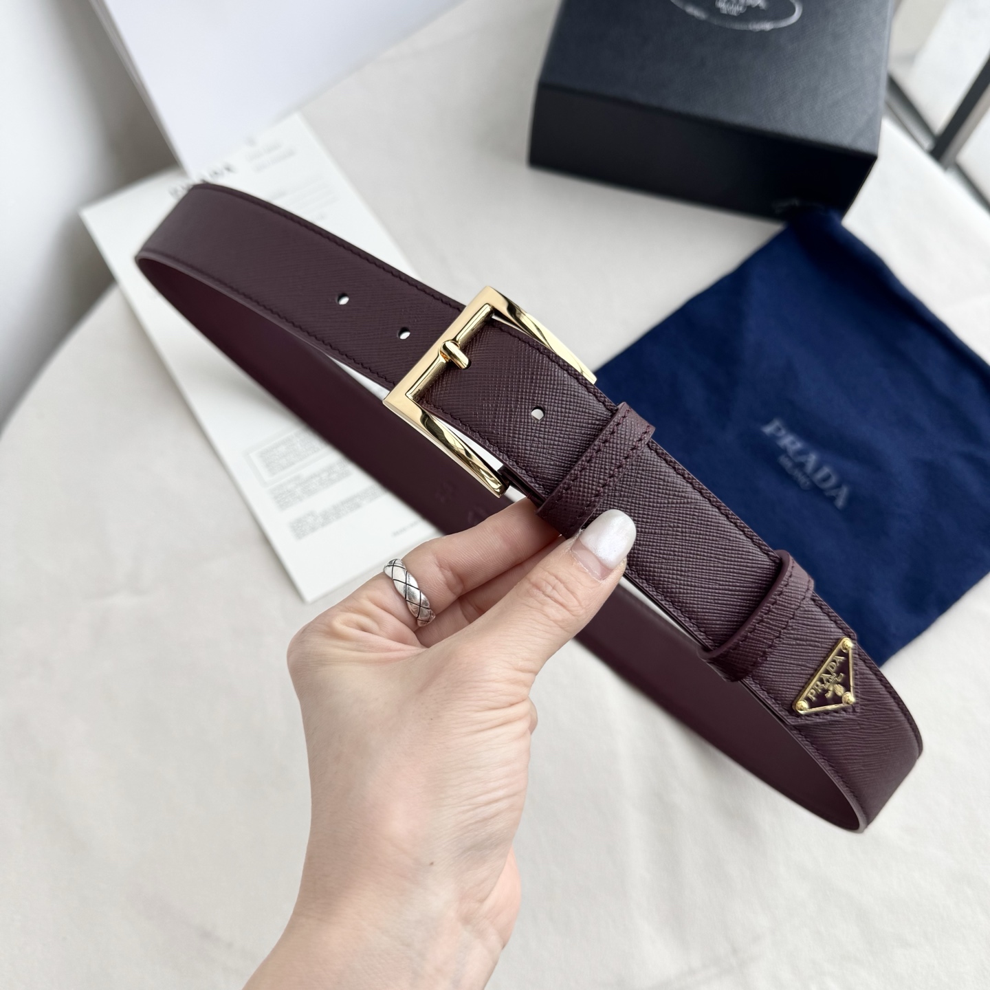 。 男女通用，P rada这款华美的十字纹牛皮腰带释放简约而精致的优雅气息 尖部的涂珐琅金属三角形徽标展