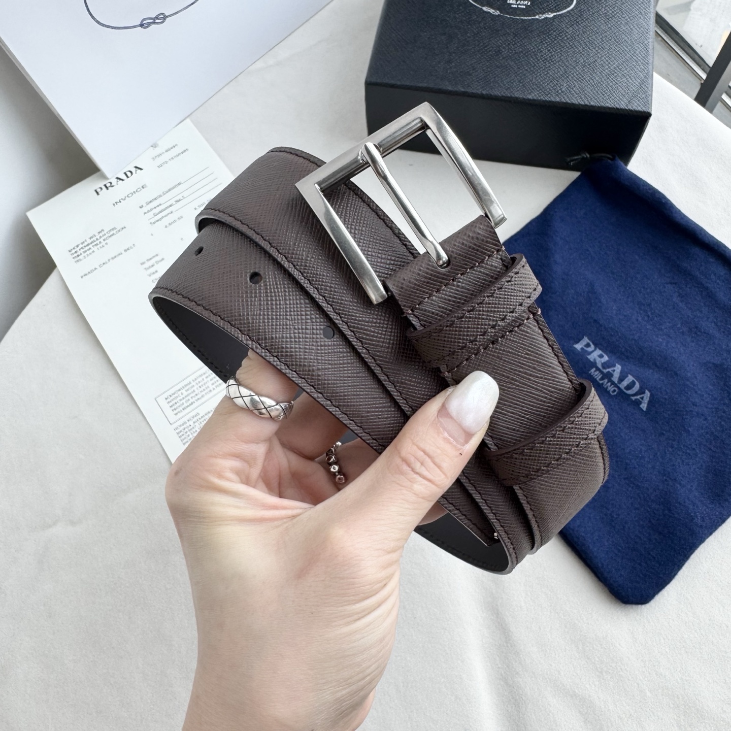 。 男女通用，P rada这款华美的十字纹牛皮腰带释放简约而精致的优雅气息 尖部的涂珐琅金属三角形徽标展