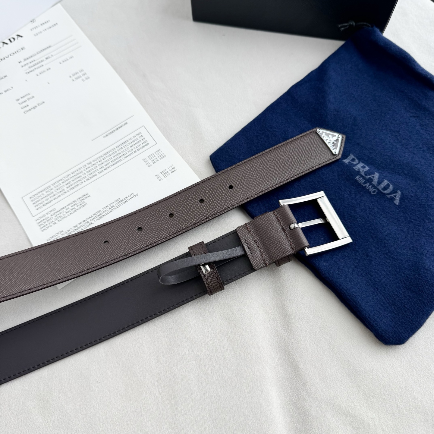 。 男女通用，P rada这款华美的十字纹牛皮腰带释放简约而精致的优雅气息 尖部的涂珐琅金属三角形徽标展