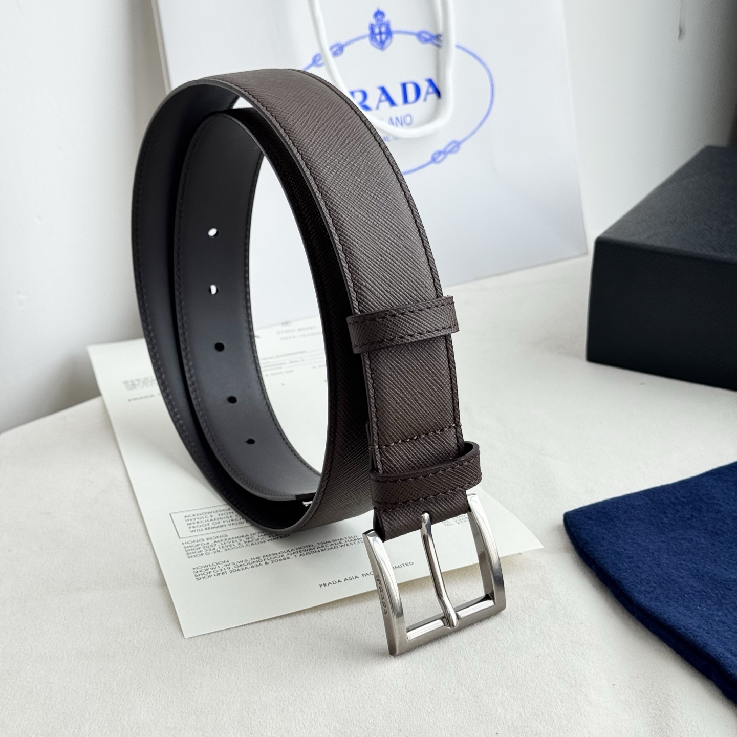 。 男女通用，P rada这款华美的十字纹牛皮腰带释放简约而精致的优雅气息 尖部的涂珐琅金属三角形徽标展