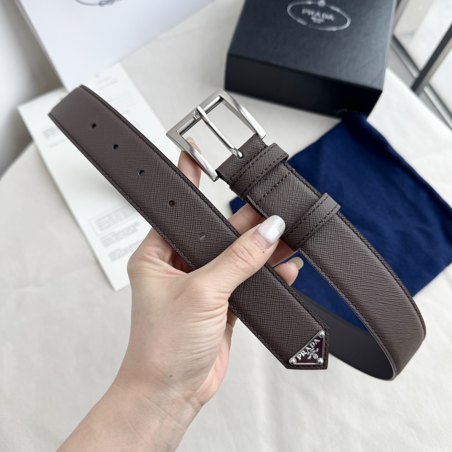 。 男女通用，P rada这款华美的十字纹牛皮腰带释放简约而精致的优雅气息 尖部的涂珐琅金属三角形徽标展
