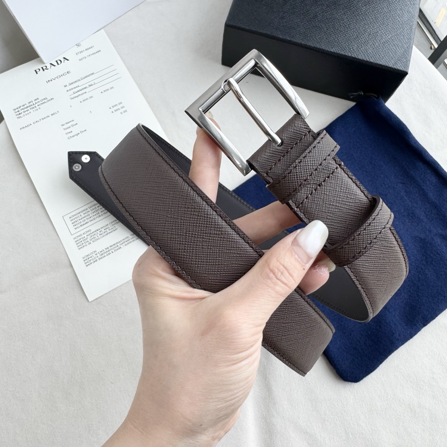 。 男女通用，P rada这款华美的十字纹牛皮腰带释放简约而精致的优雅气息 尖部的涂珐琅金属三角形徽标展