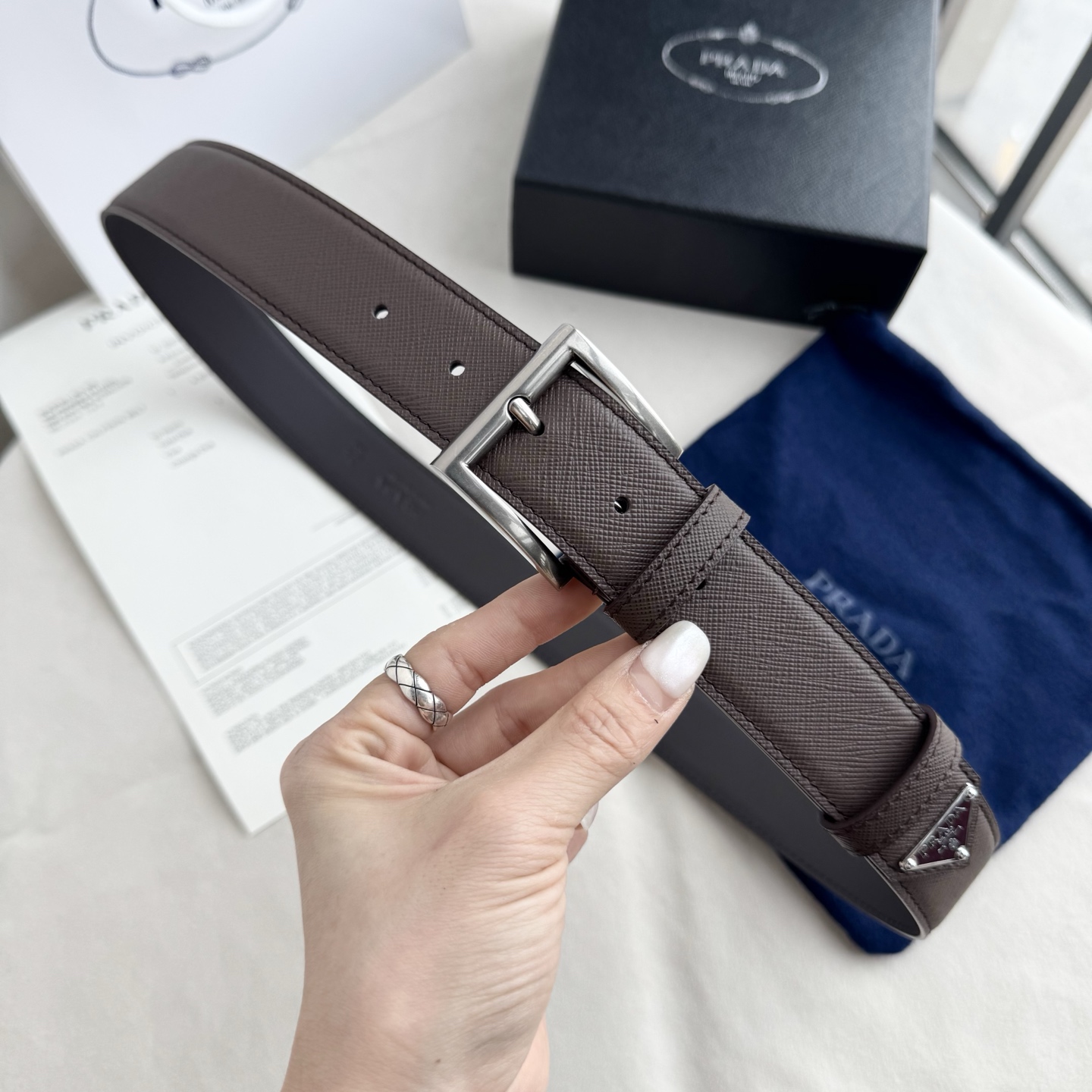 。 男女通用，P rada这款华美的十字纹牛皮腰带释放简约而精致的优雅气息 尖部的涂珐琅金属三角形徽标展