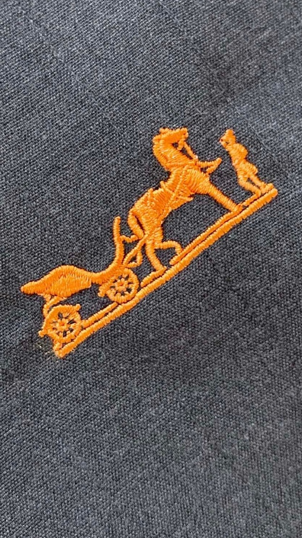 爱马仕（Hermès）高端面料和低调奢华的设计著称。左胸橙色Caleche（凯来诗/马车）刺绣，是爱马仕