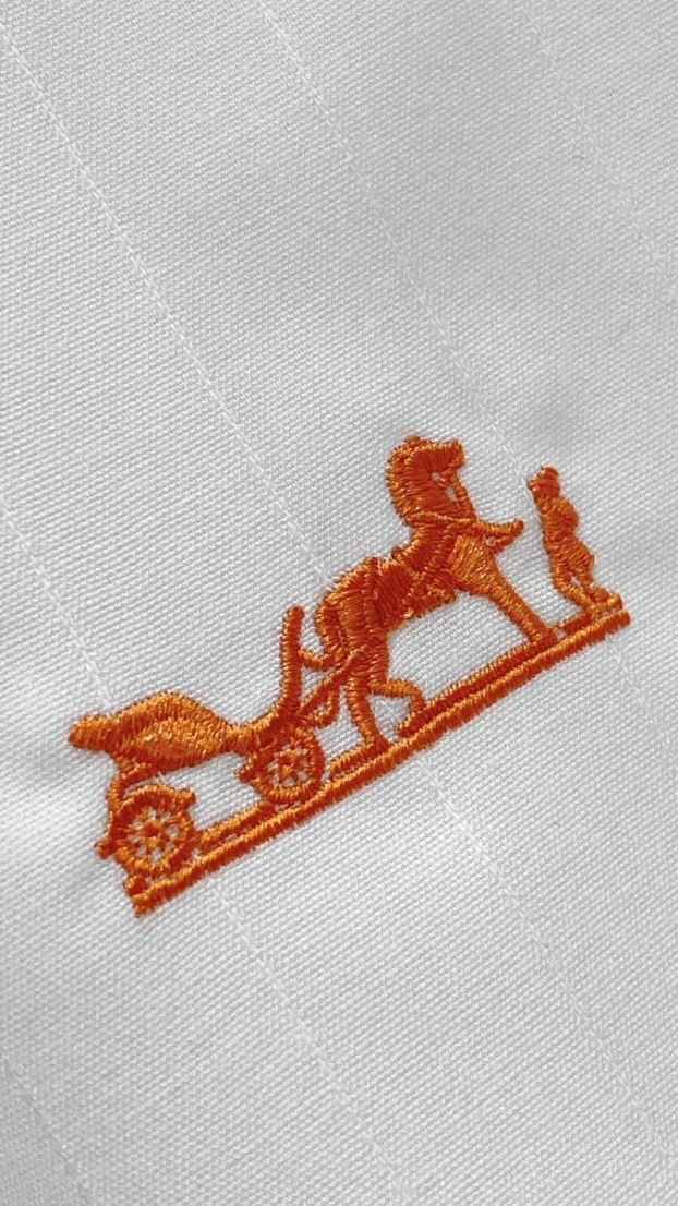 爱马仕（Hermès）高端面料和低调奢华的设计著称。左胸橙色Caleche（凯来诗/马车）刺绣，是爱马仕