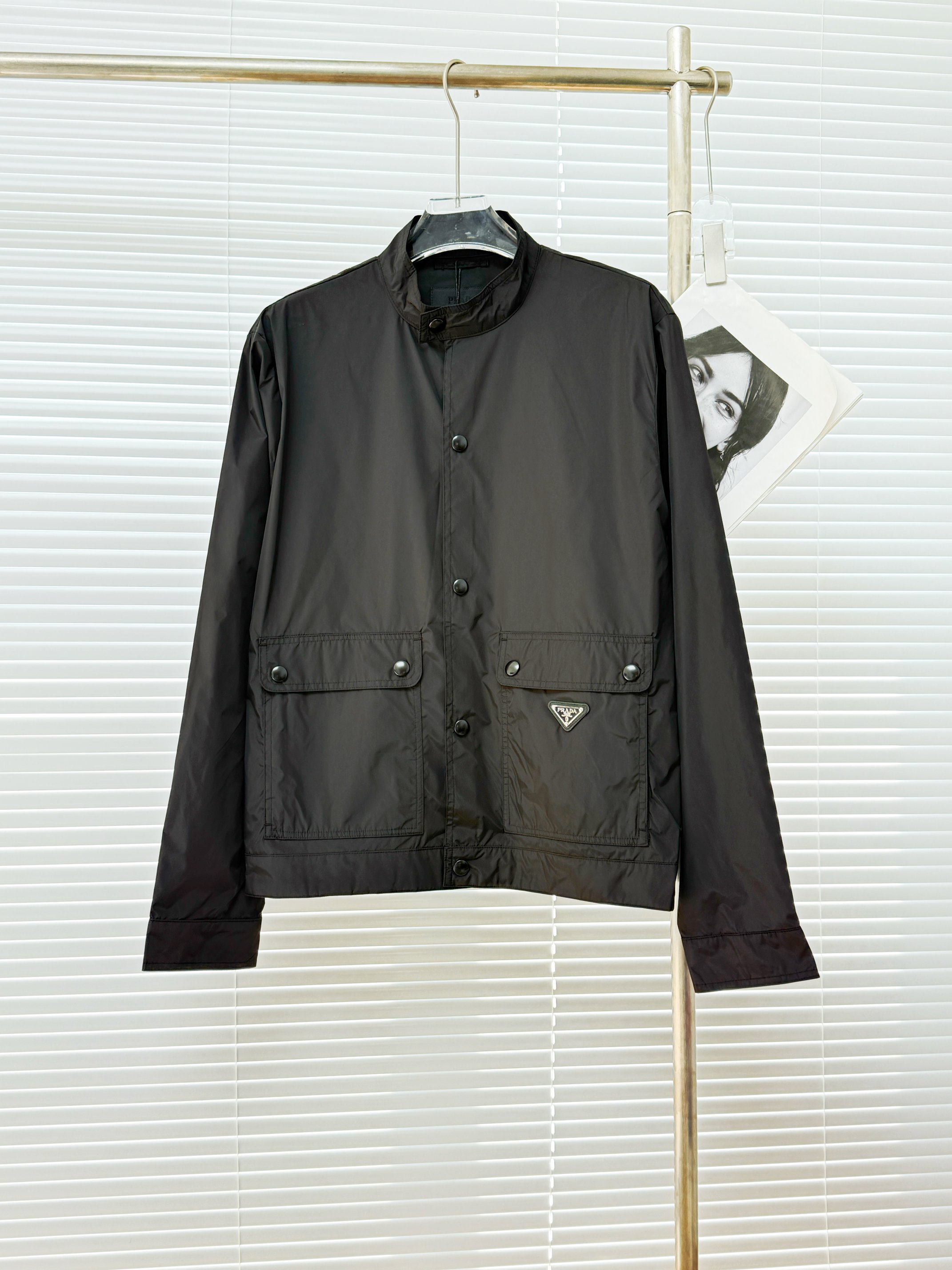 NO:954519,Prad's regenerated nylon jacket uses the brand's iconic regenerated nylon fabric, which has the same performance as traditional nylon and has high strength, tear resistance, abrasion resistance and other properties. It is lightweight and waterproof, suitable for many scenes. It is anti-wrinkle and quick-drying and is easy to care for and maintain on a daily basis.  The unlined single-layer structure relies on the high-density weaving characteristics of regenerated nylon to make it both breathable and protective. It adopts a stand-up collar structure to fit the neck line, taking into account windproof function and smart temperament. It is equipped with extra-large capacity flap pockets on both sides to enhance practicality with a three-dimensional structure, and the inner hidden pocket design improves privacy.  For a comfortable experience, both the lid and the bag are hemmed and reinforced with double-needle stitching, and an enamel-coated triangle logo is decorated on one side of the bag to enhance visual recognition. The combination of cuff straps and concealed buckles achieve precise tightness requirements, and the straight hem structure at the front of the hem and the flat rib cinch at the rear make it both aesthetically pleasing and practical.  Size M~3XL,,prada,jackets & coats,19860909Prad 再生尼龙夹克 选用品牌标志性的再生尼龙面料,与传统尼龙性能相当,具备高强度,抗撕裂,耐磨损等特性.其质地轻盈,同时又具备防水功能适合多场景需求.抗皱,快干的特点也易于日常打理维护. 无衬里单层结构,依托再生尼龙的高密度编织特性,使其透气性与防护性并存.采用立领结构,贴合颈部线条,兼顾防风功能和干练气质.两侧搭配超大容量翻盖口袋,以立体结构强化实用性,内层暗袋设计提升私密收纳体验,盖体和袋体均用双针车线工艺进行包边加固,将涂珐琅三角标饰以一侧袋体之上,强化视觉辨识度.袖口袢带与暗扣的组合实现精准松紧需求,下摆正面平直底边结构与后方的扁牛筋收口让其兼顾美感和实用性. 尺码M~3XL,,prada,jackets & coats,,Men's clothing