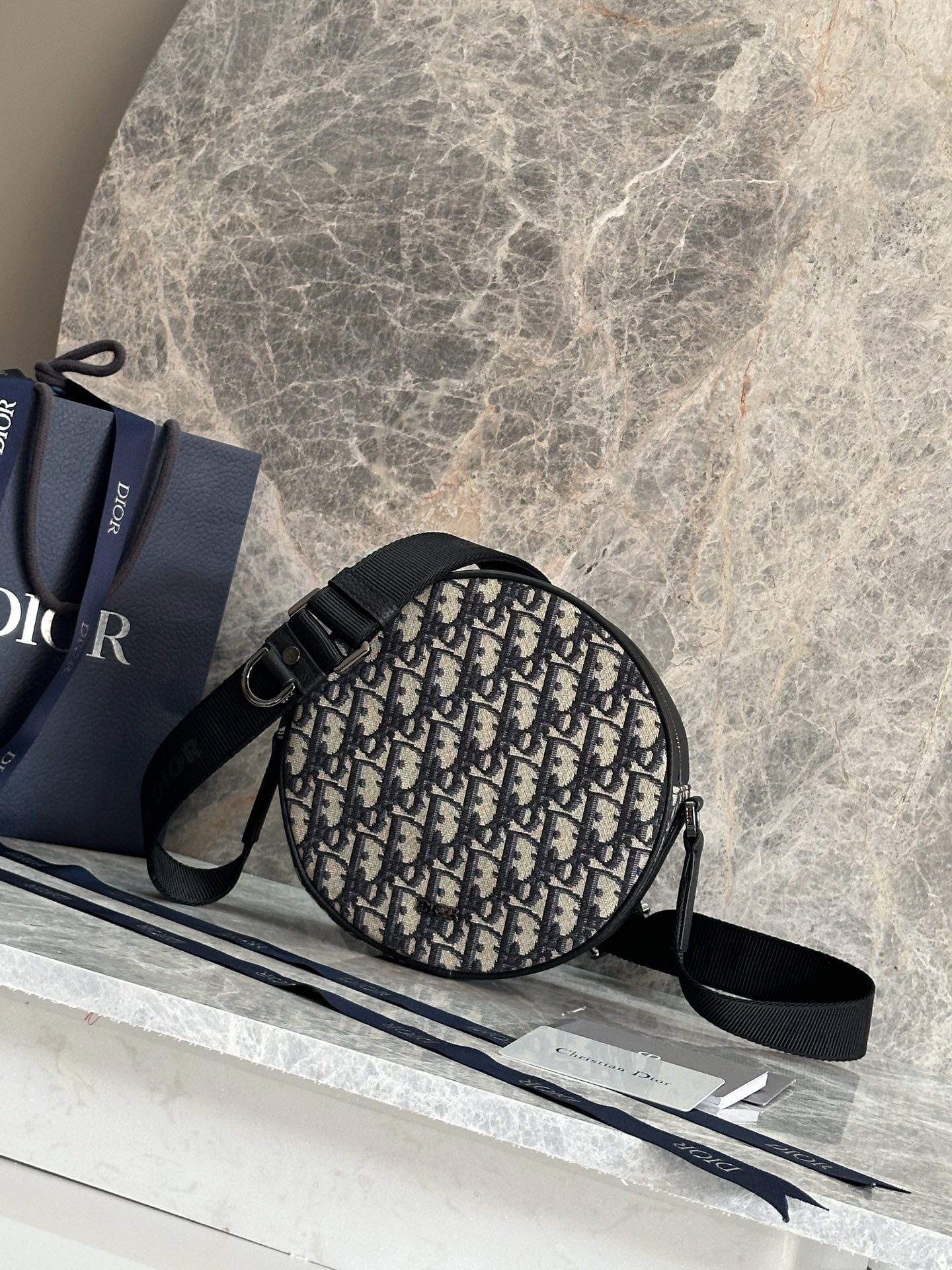 NO:395174,P This Dior Yoyo Zipper Messenger Bag is a new product for the 2025 summer men's clothing series, which is stylish and practical. The round style is carefully crafted from beige and black Oblique printed fabrics, decorated with black grained cowhide leather details to enhance the style, and the front is decorated with Dior logo. It is paired with a back insertion bag and zipper closure. The main compartment has a socket bag that can accommodate a variety of daily necessities. It is paired with an adjustable Christian Dior logo shoulder strap, which can be matched with a variety of shapes to add the finishing touch. Fabric fabric, lining fabric, decorative and decorative lines Zipper main compartment Internal pocket Back insertion bag Adjustable Christian Dior logo nylon jacquard shoulder strap is decorated with D-shaped trim, and the front is decorated with a retro silver finish copper alloy Dior logo  Dust bags included Made in Italy Dimensions 20 x 20 x 7.5 cm (Length x Height x Width) Model: 93918 Blue cloth, Dior, Dior, Dior, Cowhide19860909P 这款 Dior Yoyo 拉链信使包是二零二五夏季男装系列新品,时尚实用.圆形款式,采用米色和黑色 Oblique 印花面料等材质精心制作,饰以黑色粒面牛皮革细节提升格调,正面点缀以 Dior 标志.搭配背面插袋和拉链开合,主隔层配有一个插袋,可收纳各种日常用品.搭配可调节 Christian Dior 标志肩带,可与各式造型搭配,增添点睛之笔. 面料织物 里料织物 装饰物及装饰线除外 拉链主隔层 内部插袋 背面插袋 可调节的 Christian Dior 标志尼龙提花肩带饰以 D 形饰环 正面饰以复古银色饰面铜合金 Dior 标志 内含防尘袋 意大利制造 尺寸20 x 20 x 7.5 厘米（长 x 高 x 宽） 型号:93918蓝布,迪奥,dior,dior,cowhide,Bag