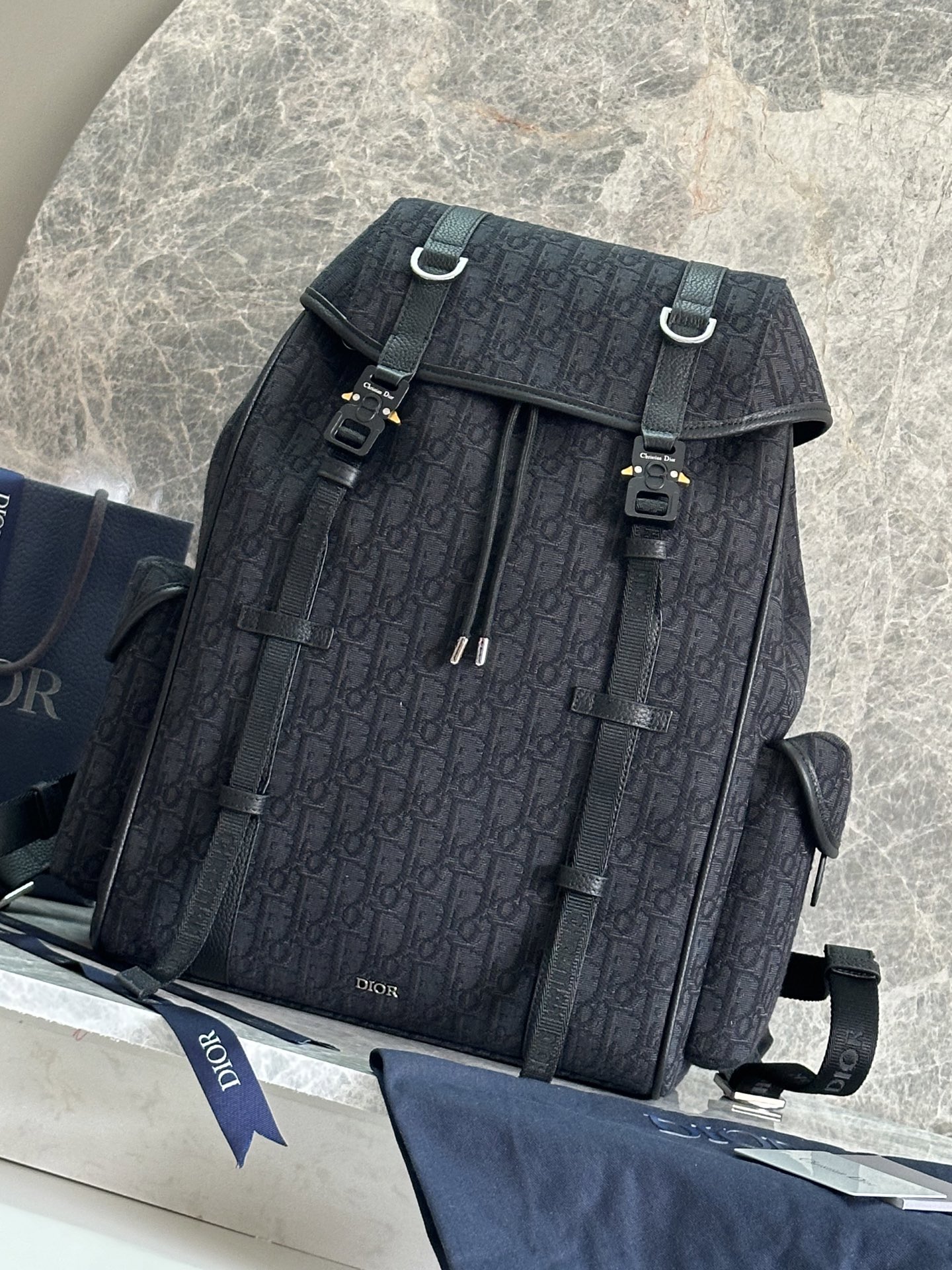 NO:213531,P This Dior Hit The Road flip backpack combines modern style with the high-order spirit of Dior. It is carefully crafted from black Oblique printed fabrics and other materials, decorated with grained cowhide leather details to enhance the style, and the front is decorated with Dior logo. The flip is paired with CD logo mini aluminum buckles and two Christian Dior logo nylon jacquard tapes. It has a spacious main compartment and two side magnetic flip pockets. It is practical and versatile, adding the finishing touch to all kinds of casual looks. Fabric fabric, lining fabric, decorative and decorative lines, main compartment is matched with flip and drawstring, tone CD logo mini aluminum buckle and D-shaped trim internal flat computer compartment Side magnetic flip pocket Top leather handle  Adjustable padded shoulder straps Padded mesh fabric on the back, decorated with Dior logo, front with metal clad copper alloy Dior logo, interior with Dior embossed logo, included dust bag Made in Italy Dimensions 43 x 43 x 18 cm (L x H x W) Main compartment can hold 1 15-inch laptop, A4 files and 1 tablet Side pockets can hold various models of mobile phone models: FK-1ESBA205YKY, Dior, dior, backpacks, cowhide19860909P 这款 Dior Hit The Road 翻盖双肩背包将现代风格与 Dior 的高订精神融为一体.采用黑色 Oblique 印花面料等材质精心制作,饰以同色调粒面牛皮革细节提升格调,正面点缀以 Dior 标志.翻盖搭配 CD 标志迷你铝扣和两条 Christian Dior 标志尼龙提花饰带,内设宽敞主隔层,搭配两个侧面磁性翻盖口袋.实用百搭,为各式休闲造型增添点睛之笔. 面料织物 里料织物 装饰物及装饰线除外 主隔层搭配翻盖和抽绳 同色调 CD 标志迷你铝扣和 D 形饰环 内部扁平电脑隔层 侧面磁性翻盖口袋 顶部皮革手柄 可调节加垫肩带 背部采用加垫网眼织物,饰以 Dior 标志 正面饰以金属覆层铜合金 Dior 标志 内部饰有 Dior 压花标志 内含防尘袋 意大利制造 尺寸43 x 43 x 18 厘米（长 x 高 x 宽） 主隔层可收纳 1 部 15 英寸笔记本电脑、A4 文件和 1 部平板电脑 侧面口袋可收纳各种型号的手机型号:FK-1ESBA205YKY,迪奥,dior,dior,backpacks,cowhide,Bag