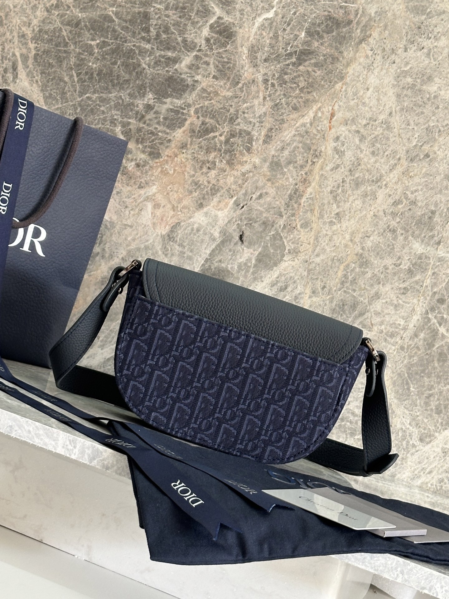   这款马鞍手拿包附有肩带，是二零二五春季男装系列推出的新款单品，采用时尚的设计，彰显精致的优雅气质，为