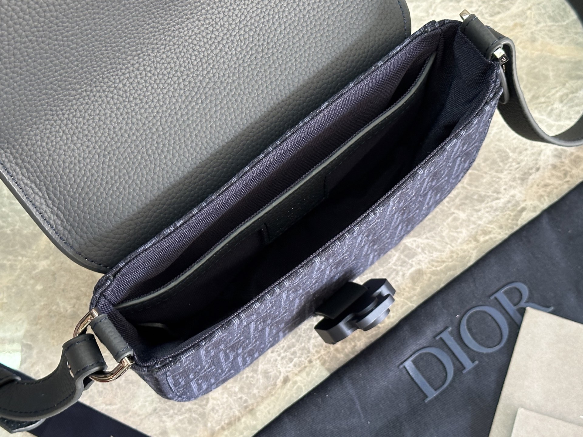   这款马鞍手拿包附有肩带，是二零二五春季男装系列推出的新款单品，采用时尚的设计，彰显精致的优雅气质，为