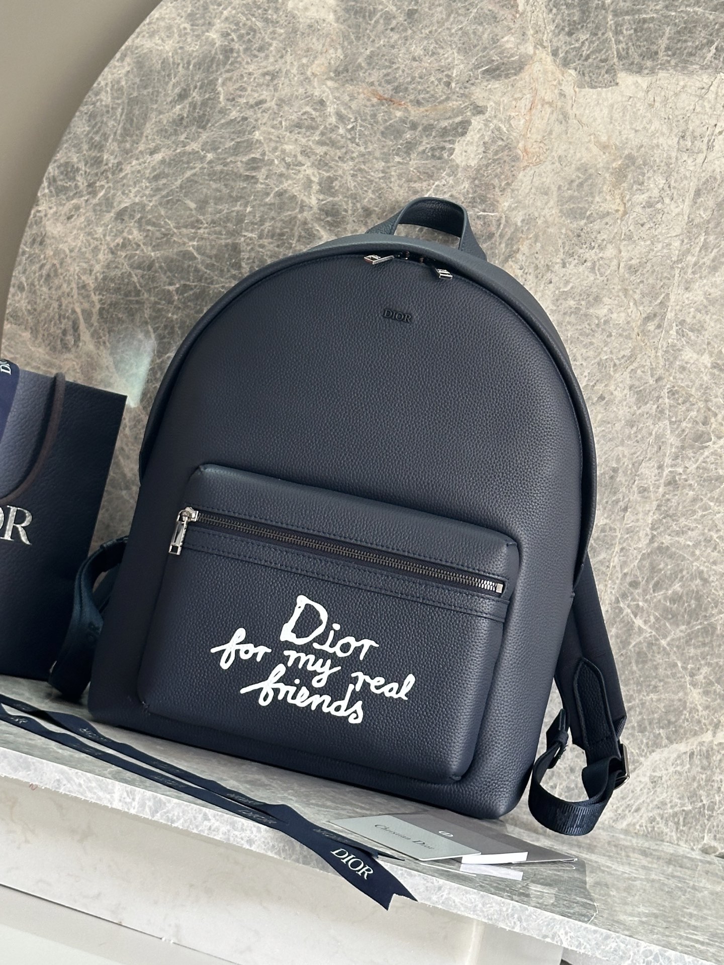 NO:386422,P This Rider 2.0 zipper backpack comes from the DIOR AND HYLTON NEL limited series. It is carefully crafted from navy blue grain cowhide leather and other materials. The large zipper pocket on the front is decorated with a white Dior For My Real Friends logo printed from the DIOR AND HYLTON NEL co-branded series to enhance the style. The zipper closure, paired with adjustable padded shoulder straps, is an ideal accessory for daily life. Model 93328 Blue Leather Size: 32x43x19cm (Length x Height x Width) The main compartment can hold 1 15-inch laptop, A4 file and 1 tablet Fabric: cowhide leather, fabric lining: fabric Decoration and decorative lines are the main compartment  Interior flat computer compartment interior insert pocket Front zipper pocket Top leather handle adjustable padded shoulder strap Back padded mesh fabric, Dior logo Front vintage silver finish copper alloy Dior logo Interior DIOR AND HYLTON NEL embossed logo contains dust bag Made in Italy, Dior, dior, backpacks, cowhide19860909P 这款Rider 2.0拉链双肩背包来自DIOR AND HYLTON NEL 限定系列.采用海军蓝色粒面牛皮革等材质精心制作,正面大号拉链口袋饰以来自 DIOR AND HYLTON NEL 联名系列的白色Dior For My Real Friends 标志印花提升格调.拉链开合,搭配可调节的加垫肩带,是日常生活的理想配饰. 型号93328蓝皮 尺寸:32x43x19厘米(长x高x宽) 主隔层可收纳1 部15 英寸笔记本电脑、A4文件和1部平板电脑 面料:牛皮革,织物里料:织物 装饰物及装饰线除外拉链主隔层 内部扁平电脑隔层内部插袋 正面拉链口袋顶部皮革手柄可调节加垫肩带 背部采用加垫网眼织物,饰以Dior 标志正面饰以复古银色饰面铜合金Dior 标志 内部饰有DIOR AND HYLTON NEL 压花标志内含防尘袋意大利制造,迪奥,dior,dior,backpacks,cowhide,Bag