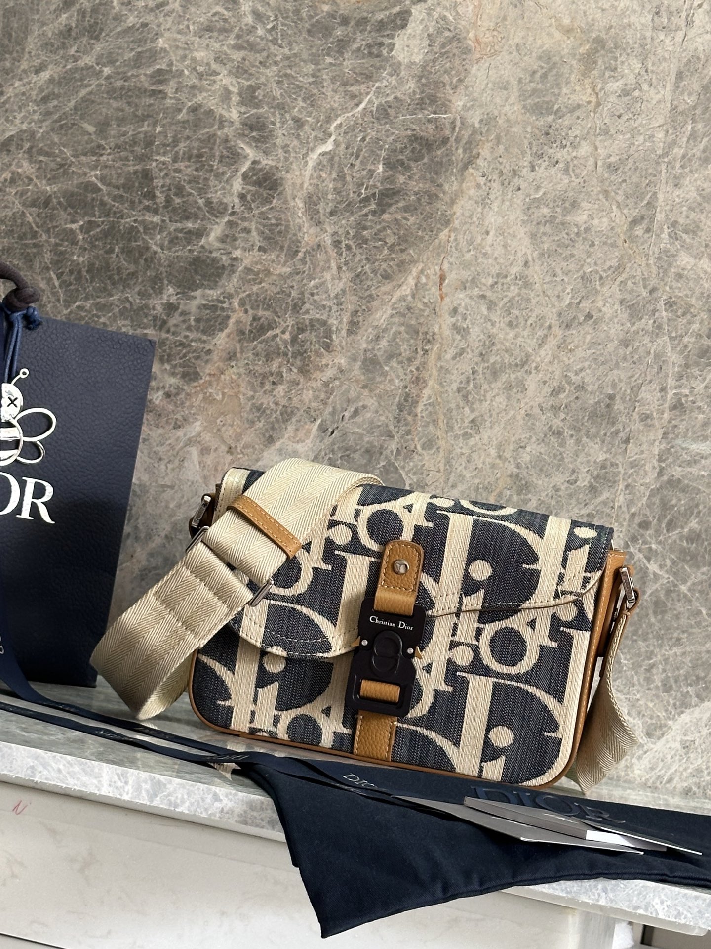 NO:395044,P This saddle messenger bag is stylish and exquisite. It is made of raffia-like Oblique printed denim fabrics and other materials, decorated with blue jacquard embroidery and contrasting beige stitching, a new interpretation of Dior classic style. Decorated with brown grain cowhide details, saddle flap, and aluminium buckle to enhance style. The spacious interior has a socket bag that can hold a variety of daily necessities, with herringbone pattern adjustable shoulder straps to enhance style, which can be shoulder or crossbody. Body cotton, cowhide, technology fabric Lining tech fabric, cotton, cowhide leather Main compartment with saddle flap and CD aluminum buckle Internal insert bag Back insert bag Adjustable herringbone pattern shoulder straps with leather details Metal cladding metal accessories Dior embossed logo Inside dust bag Made in Italy  Dimensions 24 x 16.5 x 5.5 cm (Length x Height x Width) Carrying various models of mobile phones Strap length 85 - 131 cm Strap top to top of handbag length 37 - 61 cm Weight 638 g Dimensions and weight details may vary depending on product material No.: 93932 Brown, Dior, Dior, Dior, Cowhide19860909P 这款马鞍信使包款式时尚精巧.采用酒椰草效果 Oblique 印花牛仔面料等材质精心制作,饰以蓝色提花刺绣,点缀以对比鲜明的米色缝线,全新演绎 Dior 经典款式.饰以棕色粒面牛皮革细节,搭配马鞍翻盖,点缀以铝扣提升格调.宽敞的内部空间设有一个插袋,可收纳各种日常用品,搭配人字形图案可调节肩带提升格调,可肩背或斜挎. 主体棉,牛皮革,科技面料 里料科技面料,棉,牛皮革 主隔层搭配马鞍翻盖和 CD 铝扣 内部插袋 背面插袋 可调节的人字形图案肩带,饰以皮革细节 金属覆层金属配件 内部饰有 Dior 压花标志 内含防尘袋 意大利制造 尺寸24 x 16.5 x 5.5 厘米（长 x 高 x 宽） 可收纳各种型号的手机 肩带长度85 - 131 厘米 肩带顶端至手袋顶端长度37 - 61 厘米 重量638 克 尺寸和重量详情可能因产品材质而有所不同 编号: 93932棕色,迪奥,dior,dior,cowhide,Bag