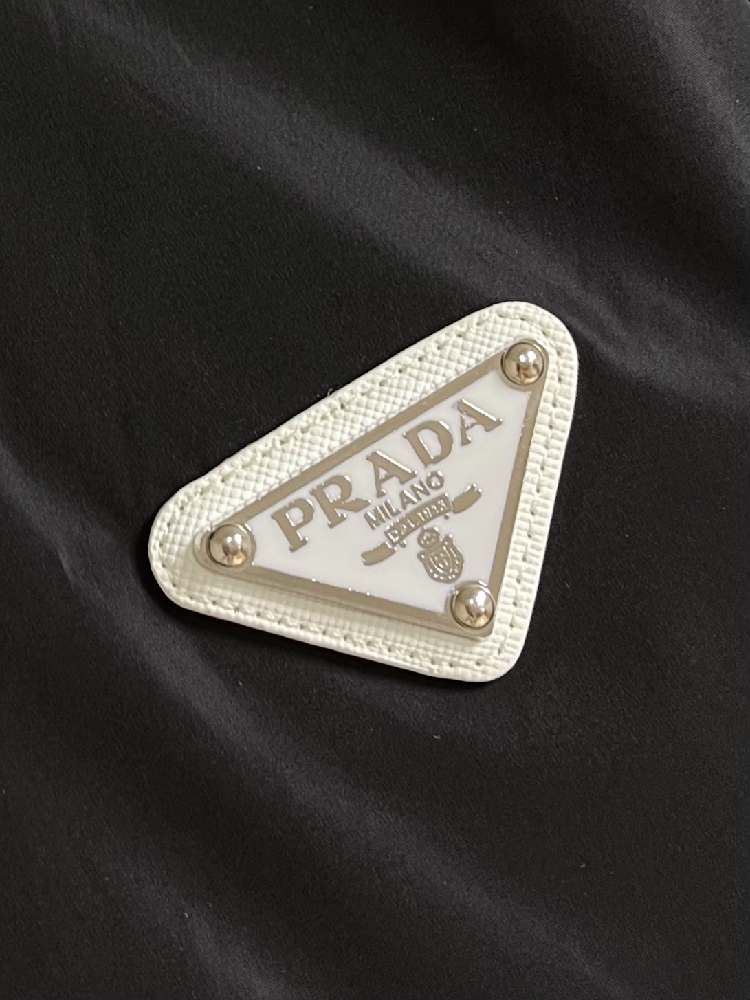 
PRADA 三角标再生尼龙外套，采用标志性的面料，是一种通过回收海洋中的塑料材料制成的再生尼龙织物体，