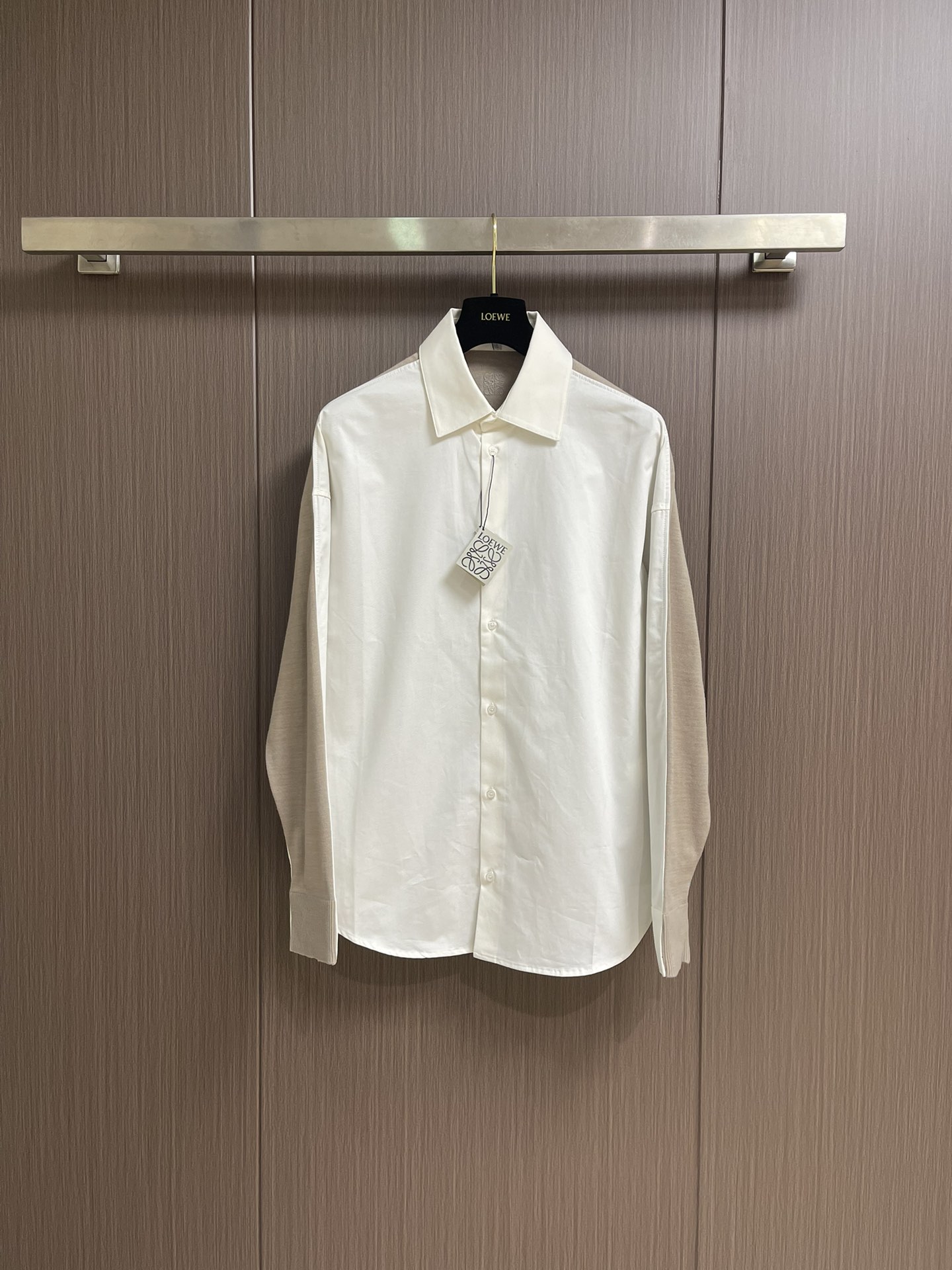 NO:540710,LOEWE  The front piece is made of high-strength cotton yarn and is made of a thin and extremely breathable fabric through a weaving process with high warp and low weft density. The surface is smooth and smooth, and the touch is as smooth as silk. At the same time, the cotton is natural skin-friendly and comfortable. Because the warp yarns are tightly arranged, the surface of the fabric has a longitudinal texture and soft luster, which enhances the visual sense of high-level. The back web is made of high-strength spinning technology and is woven into a moderately dense fabric with soft touch, which is soft and skin-friendly, and has a delicate velvet feel. The wool fiber has a natural hollow structure, which can lock in stationary air and form an excellent heat insulation layer. Even if it is light and thin, it has a good warmth effect. The head and needle are controlled by the high-precision calculation system of the embroidery machine under the back collar.  The joint operation of the rod and spool is carried out accurately in horizontal and vertical directions to form a stitch track, adjust the tension of the upper and lower lines to ensure that the stitch is flat and has no floating lines, forming an anagram embroidery with an error of ±0.1mm. The ironing master turns the collar straight, irons from the bottom to the upper end through high temperature and humid steam, applies pressure to smooth the wrinkles, and then turns to the front and repeat the operation. Turn to the collar and iron it into a curve, and press the collar to the bottom to maintain a firmness. The rotator cuff part uses the suspension method to avoid crushing the edges. After adjusting the fiber density through the ironing master's 'push, return, and pull' technology, it can better fit the human body curve. Size 36-38-40-42,,loewe,loewe,shirts,alexander  wang19860909LOEWE 罗意威拼接针织衬衫,前片选用高支棉纱通过经密高,纬密低的织造工艺制成轻薄且具有极佳透气性的面料.表面光滑平整,触感如丝绸般柔滑,同时保留棉的天然亲肤性,贴身舒适无异样感.因经纱紧密排列,织物表面呈现纵向纹理与柔和光泽,强化视觉高级感.后幅通过高支纺纱技术,用极细的羊毛纱线织成密度适中的面料,触感柔软亲肤,表面有细腻的绒感.羊毛纤维特性具有天然的中空结构,能锁住静止空气,形成绝佳的隔热层,即使轻薄,也有良好的保暖效果.后领下方处通过绣花机高精度的计算系统控制机头、针杆、线轴的协同作业,布料框架在水平和垂直方向精准移动,形成针迹轨迹,调整上线和下线张力,确保线迹平整无浮线,形成误差在±0.1mm的anagram刺绣.熨烫师将衣领翻立,通过高温湿蒸汽从底部向上端熨烫,施加压力抚平褶皱,再翻至正面重复操作.转至领口烫出弧形,后领压至最底以保持挺括.肩袖部分利用悬空法避免压死边缘.通过熨烫师的'推、归、拔'技术调整纤维密度之后,使更好的贴合人体曲线.尺码36-38-40-42,,loewe,loewe,shirts,alexander wang,Men's clothing