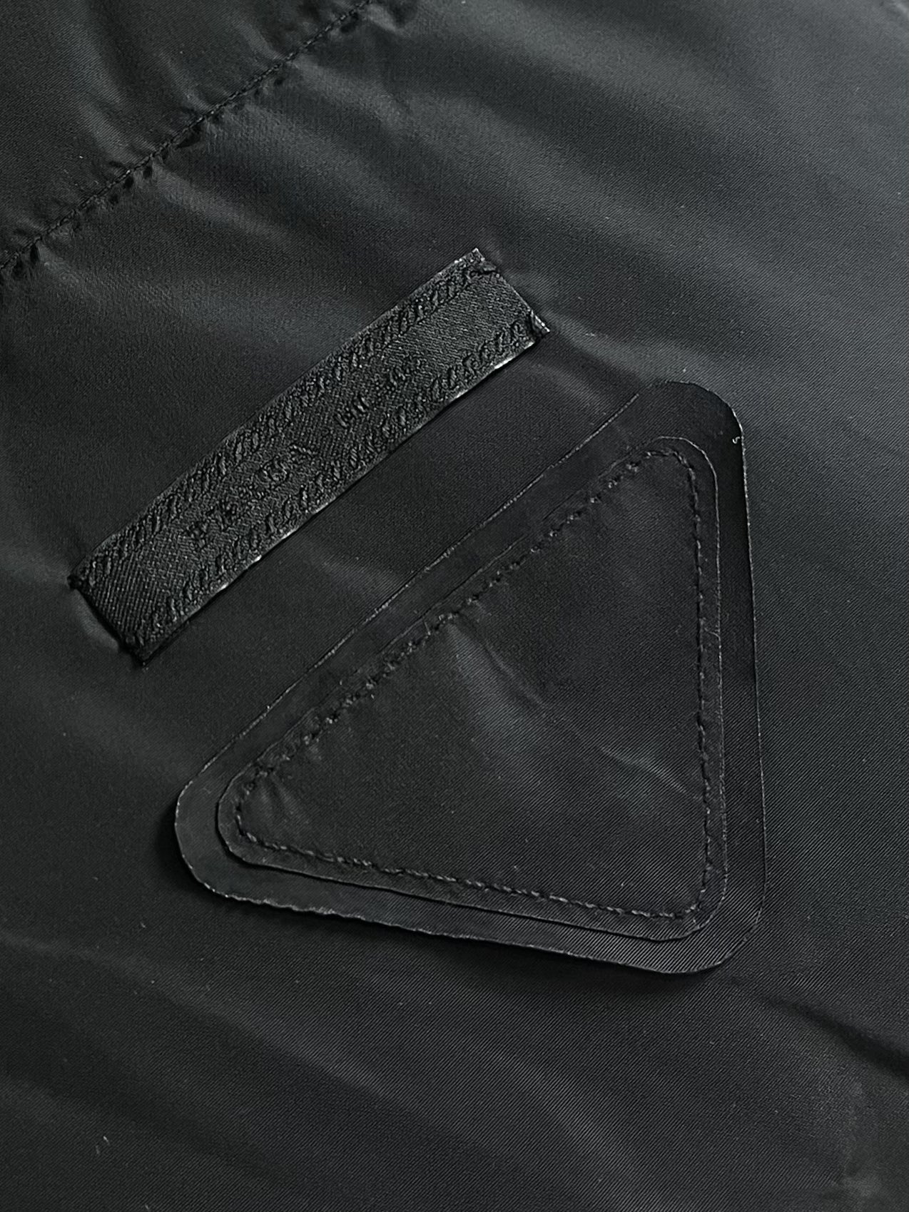 Prada 饰织物三角标羽绒马甲，选品牌标志性的再生尼龙面料，与传统尼龙性能相当，具备高强度，抗撕裂，耐