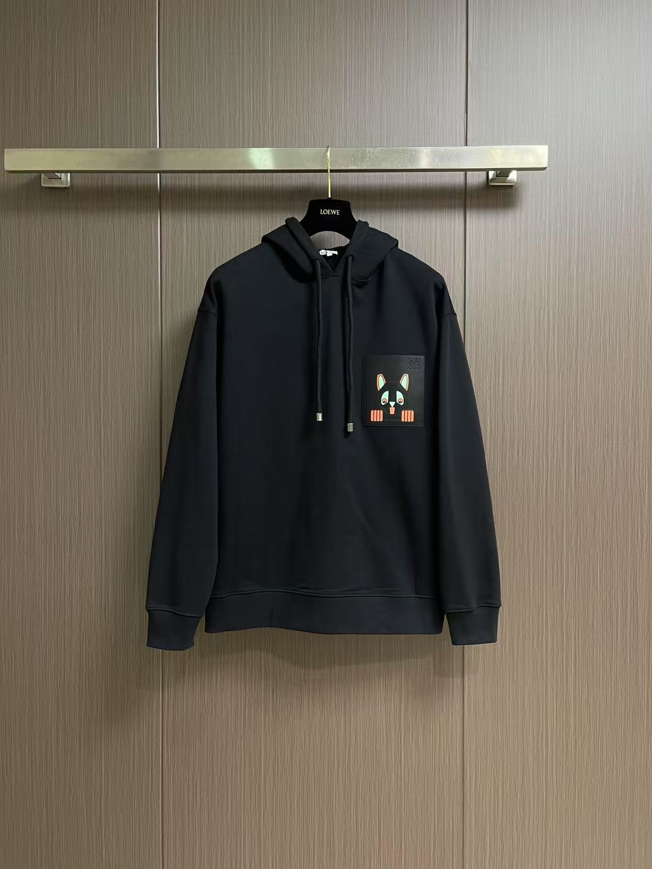 NO:645105,Loewe 2026SS early spring new style Louis Wain co-branded leather printed pocket hooded sweatshirt, made of the brand's iconic medium-weight cotton fleece as the main fabric. Decorated with leather patch pockets on the chest. The bag surface adopts Louis Wain's 'Futuristic Cat' cartoon intarsia pattern. The color scheme is black and gray as the base, embellished with fluorescent orange, mint green and other jumping colors. The bag body is also embossed with the brand logo, which not only retains the texture of the leather craftsmanship, but also strengthens the recognition of the joint series.  The version is loose cut + standard length, with classic structures such as drawstring hood and ribbed cuffs and hem. It combines casual comfort with the sophistication of luxury items. Sizes XS-L, Louis Vuitton, loewe, loewe, hoodie, sweatshirts, hats, alexander wang19860909Loewe 罗意威 2026SS早春新款 Louis Wain联名 皮质印花口袋连帽卫衣,以品牌标志性的中克重棉质抓绒为主体面料 胸前装饰皮革贴袋 袋面采用Louis Wain'未来主义猫'卡通嵌花图案 配色以黑灰为底,点缀荧光橙、薄荷绿等跳脱色调 袋身还压印了品牌标识,既保留皮革工艺的质感,又强化了联名系列的辨识度 版型为宽松剪裁＋标准衣长 搭配抽绳连帽、罗纹袖口下摆等经典结构 兼顾休闲舒适度与奢侈单品的精致度.尺码XS-L,,louis vuitton,loewe,loewe,hoodie,sweatshirts,hats,alexander wang,Men's clothing